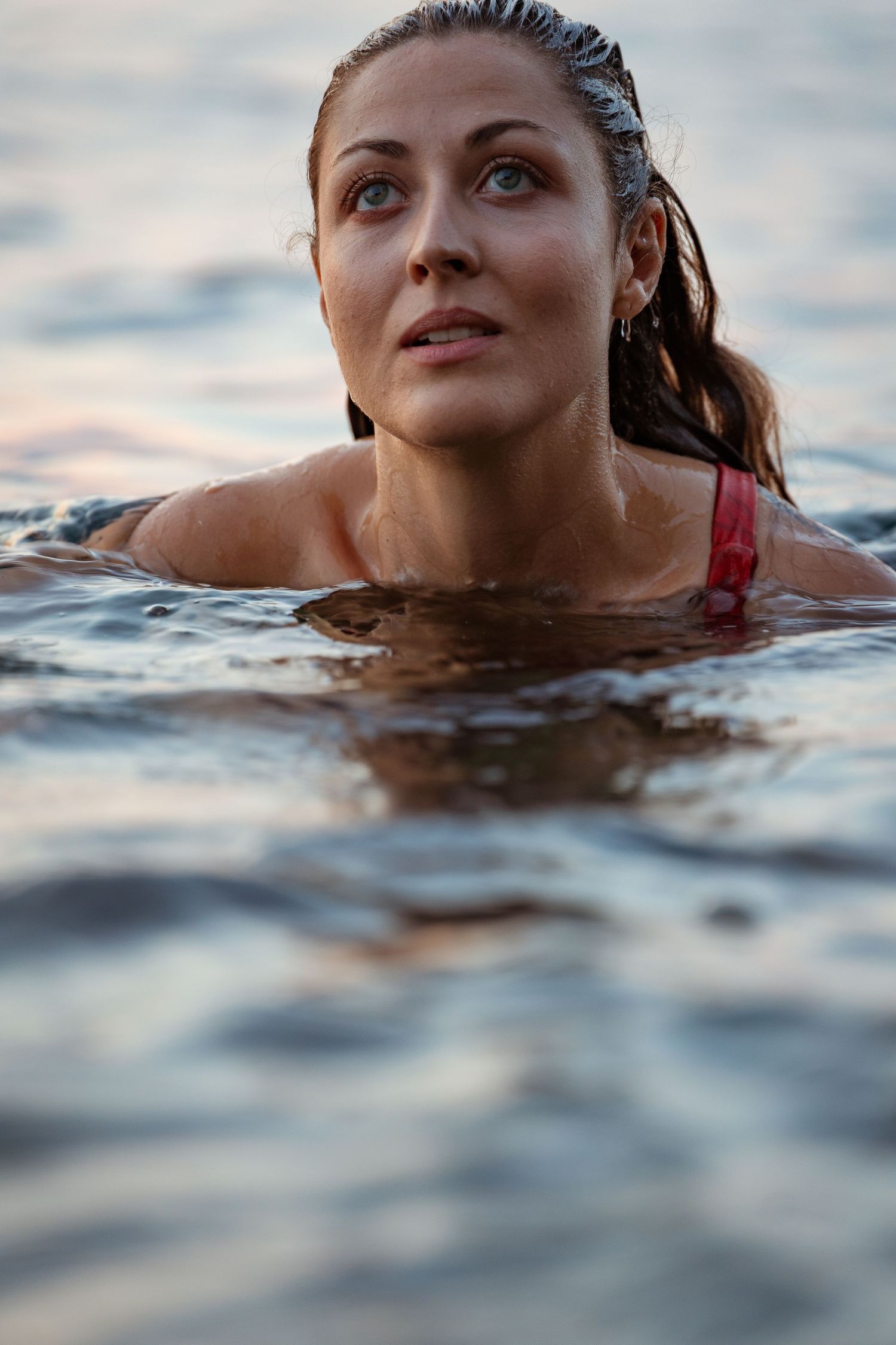 Woman with wet hair swimming in ocean water looking upward at dusk.