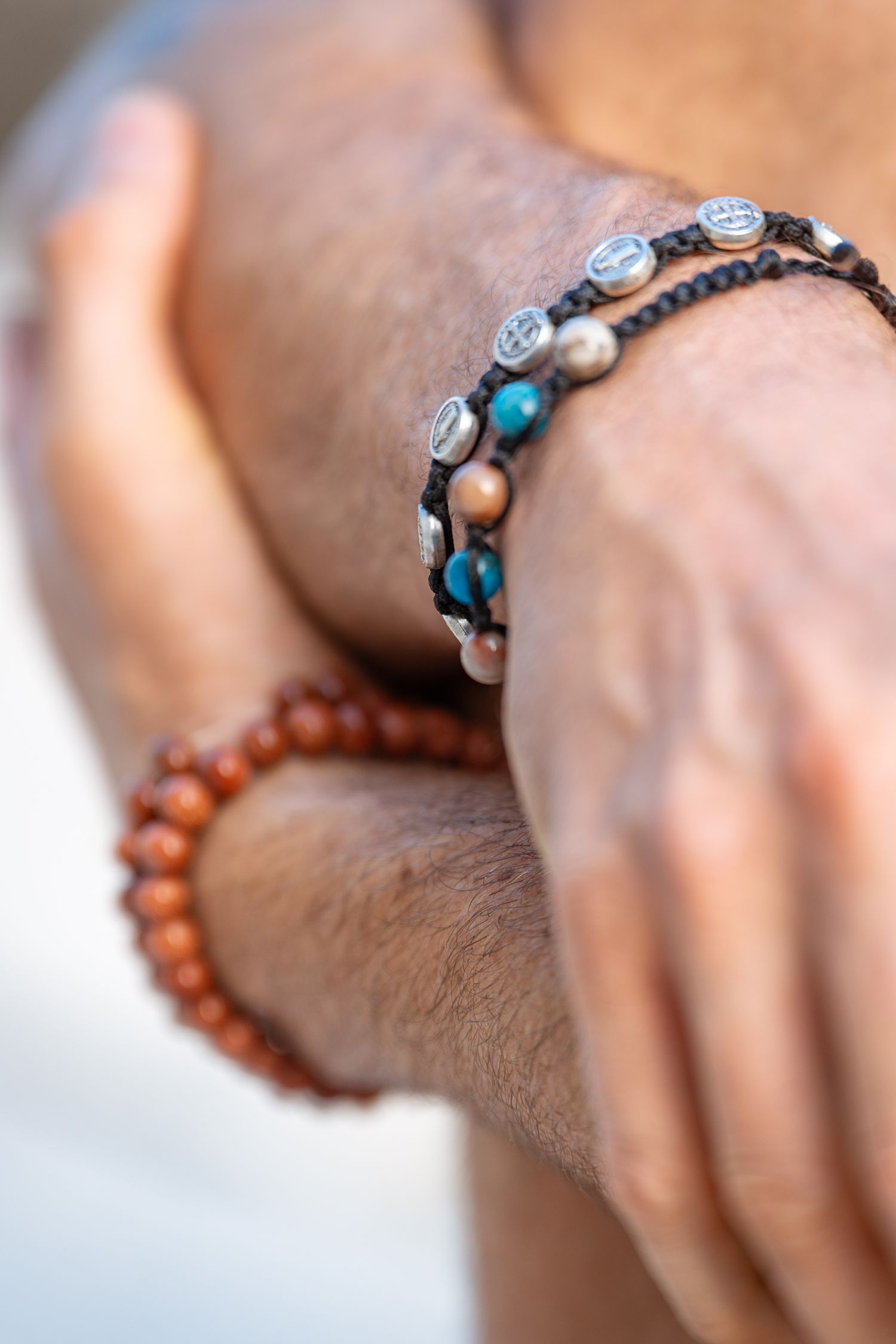 Close-up of male wrists wearing multiple beaded and charm bracelets including turquoise and brown beads.
