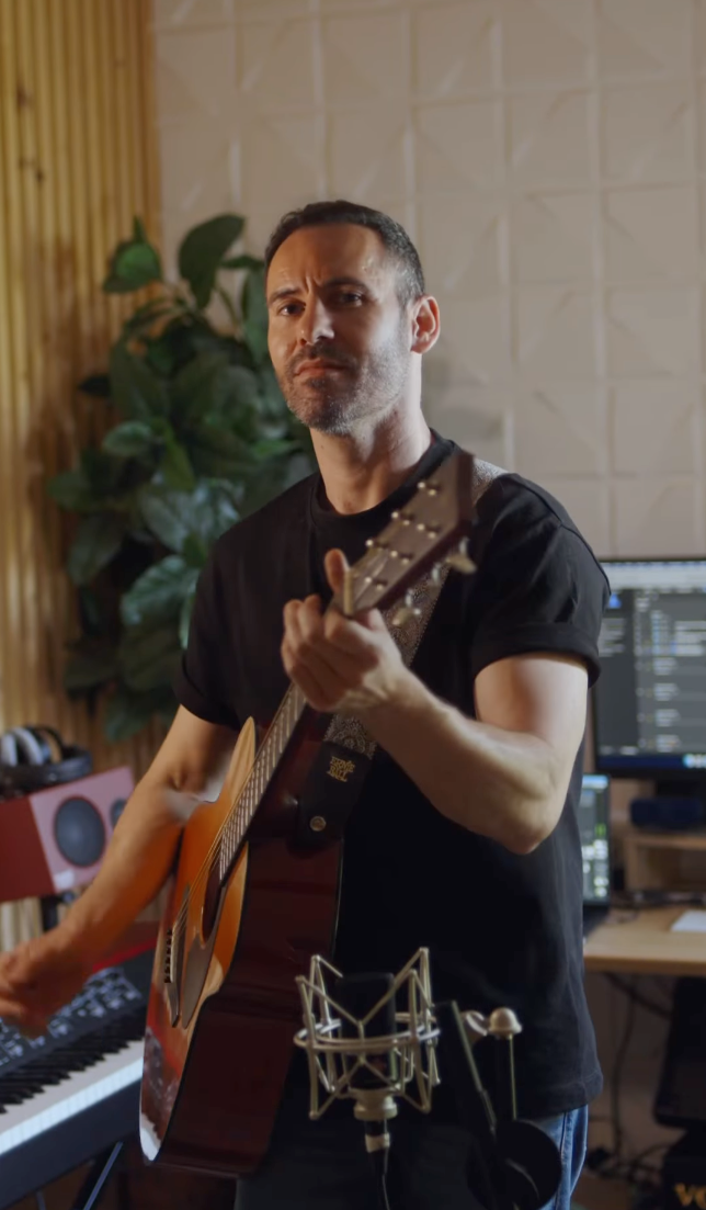 Man in black t-shirt playing acoustic guitar in music recording studio.