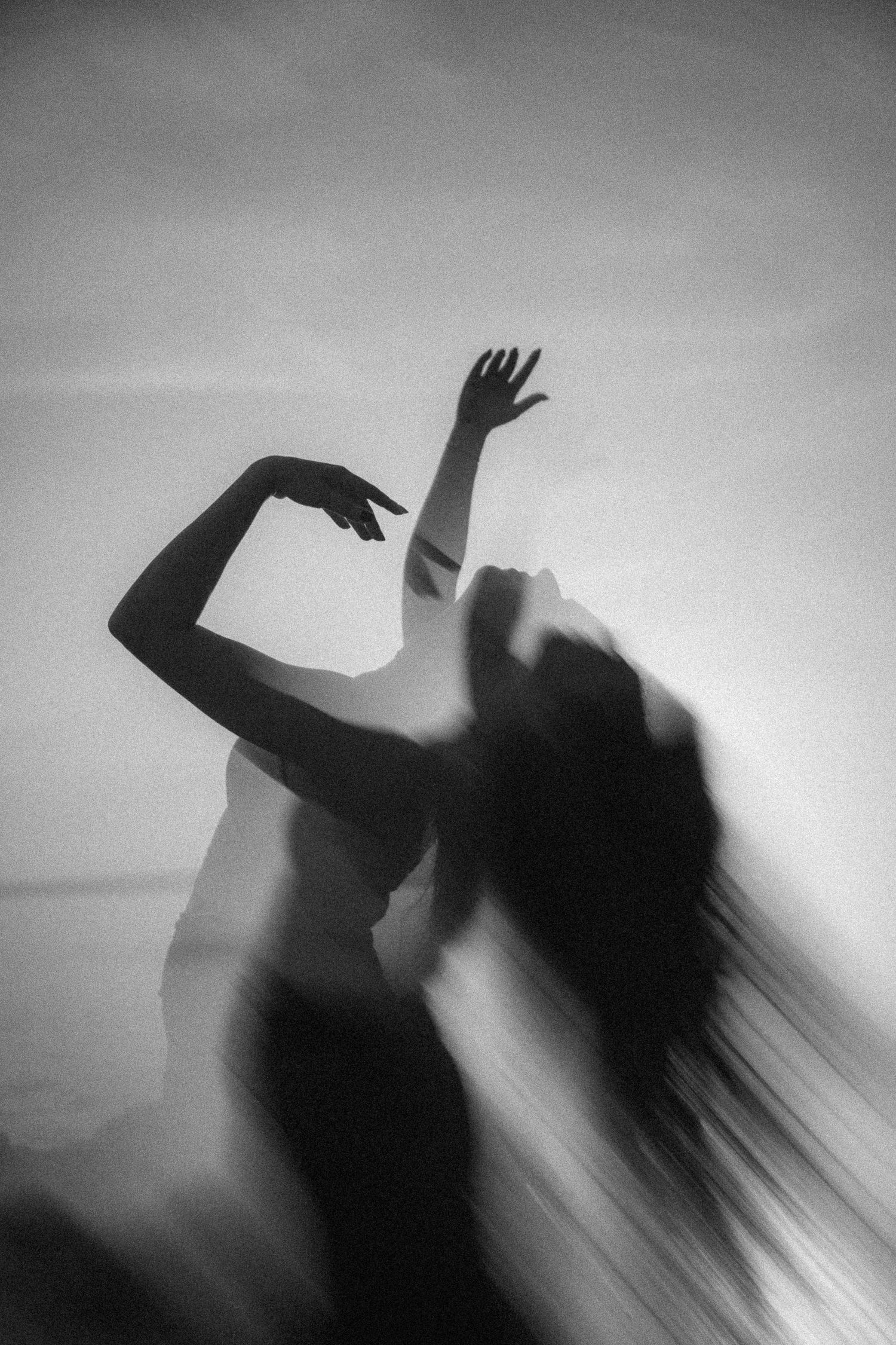 Black and white silhouette of a woman dancing with flowing hair and raised arms in misty light.