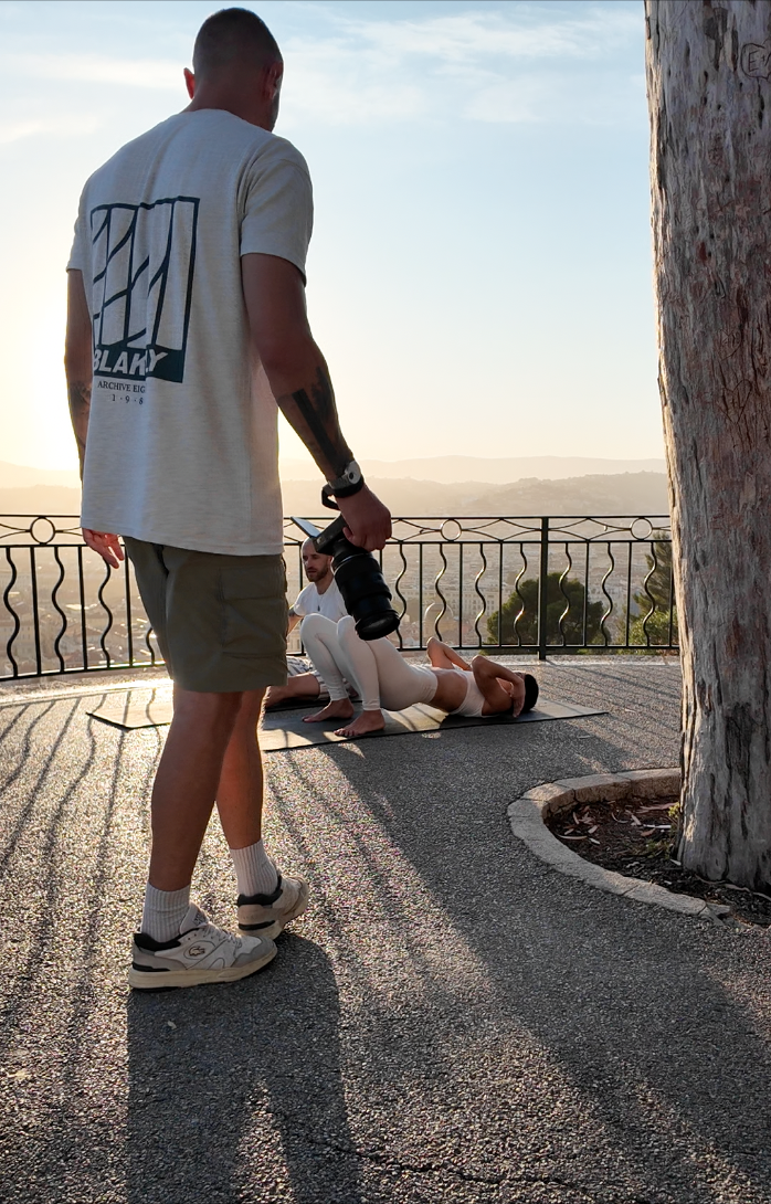 Fitness trainer using massage gun on client doing push-ups outdoors at sunrise with scenic valley view.