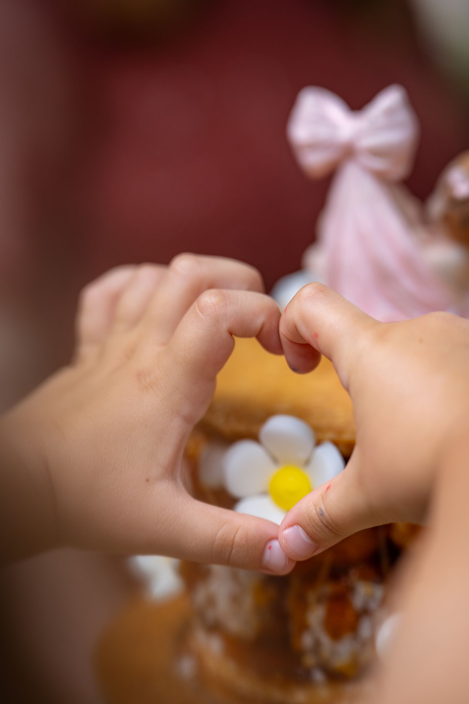 Child hands forming a heart shape in front of a decorated celebration cake with flowers.