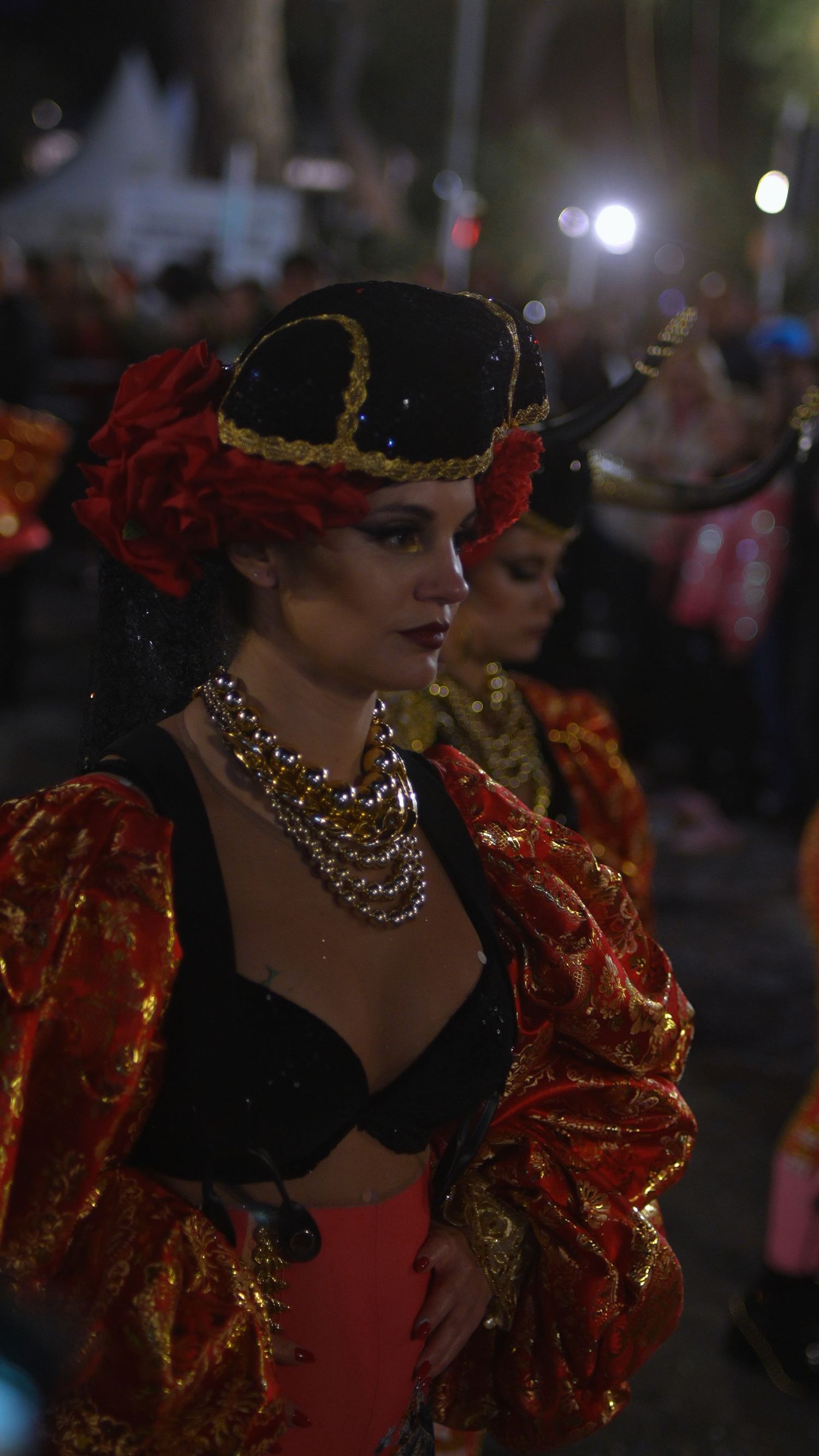 Woman in ornate red and black carnival costume with decorative hat at night.
