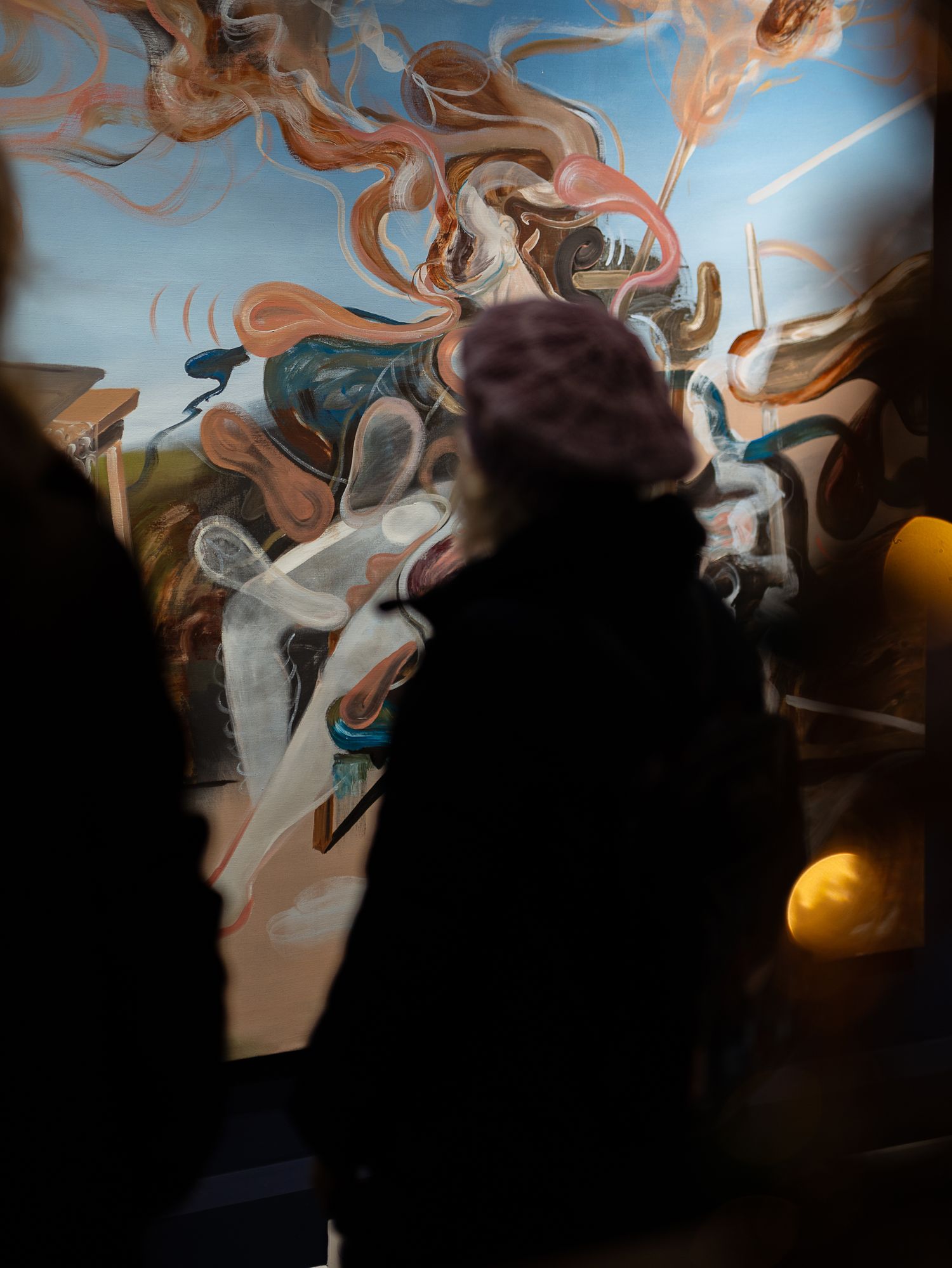 Silhouette of person in beanie viewing vibrant swirling abstract mural with smoke effects.