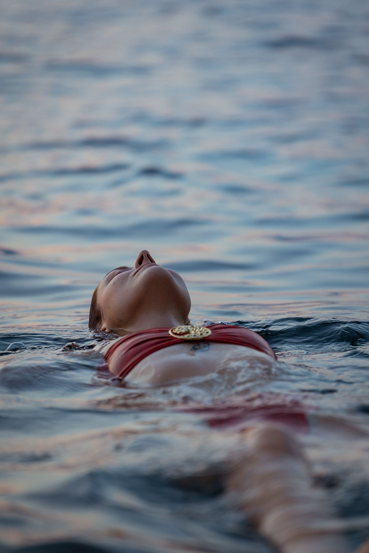 Woman in red bikini floating peacefully on her back in calm ocean water.