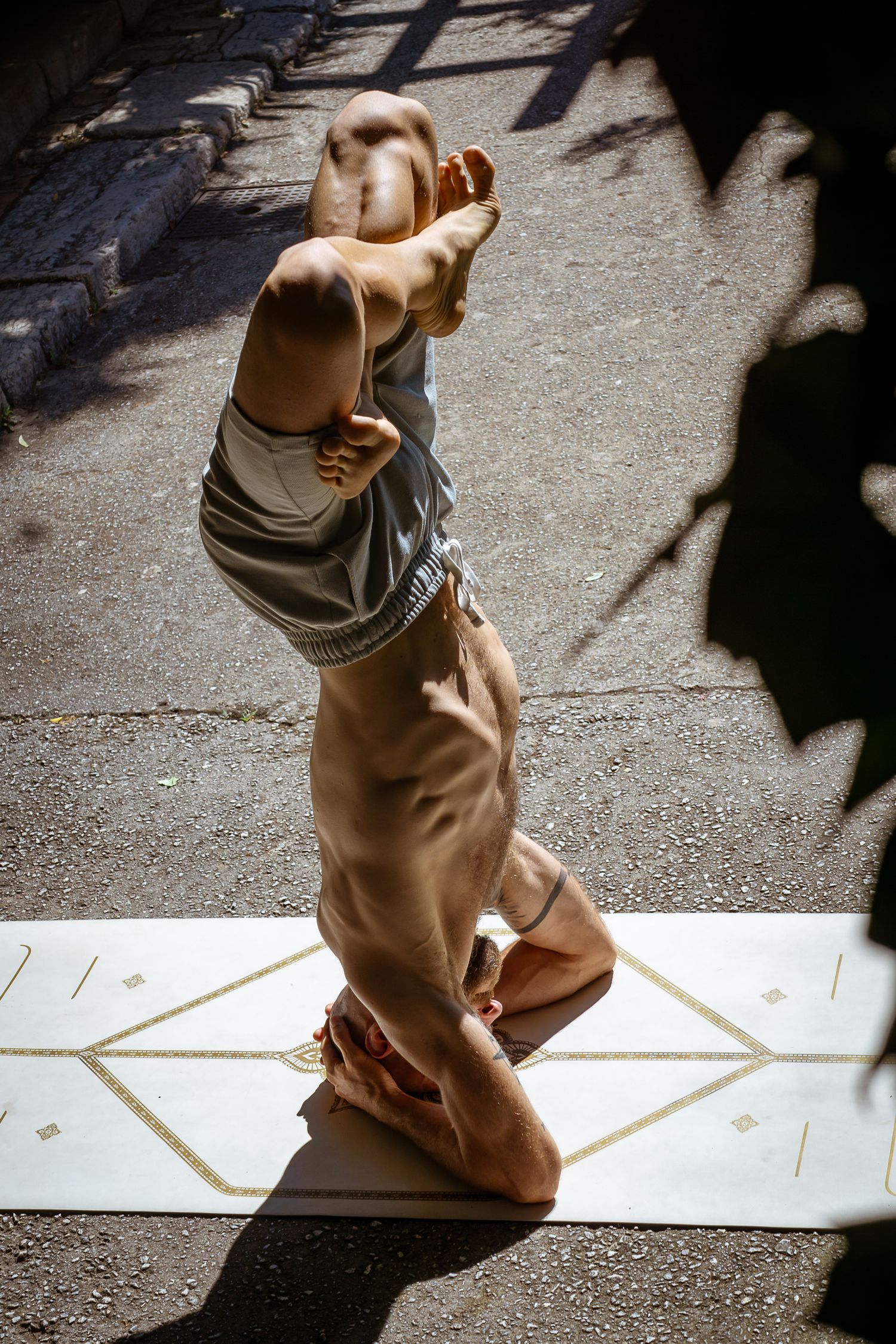 Person performing a headstand yoga pose on a mat outdoors in sunlight.