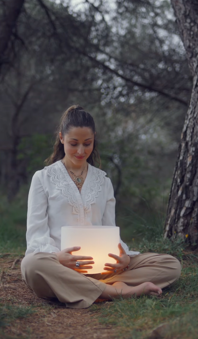 Woman sitting cross-legged in forest holding a glowing illuminated cube.