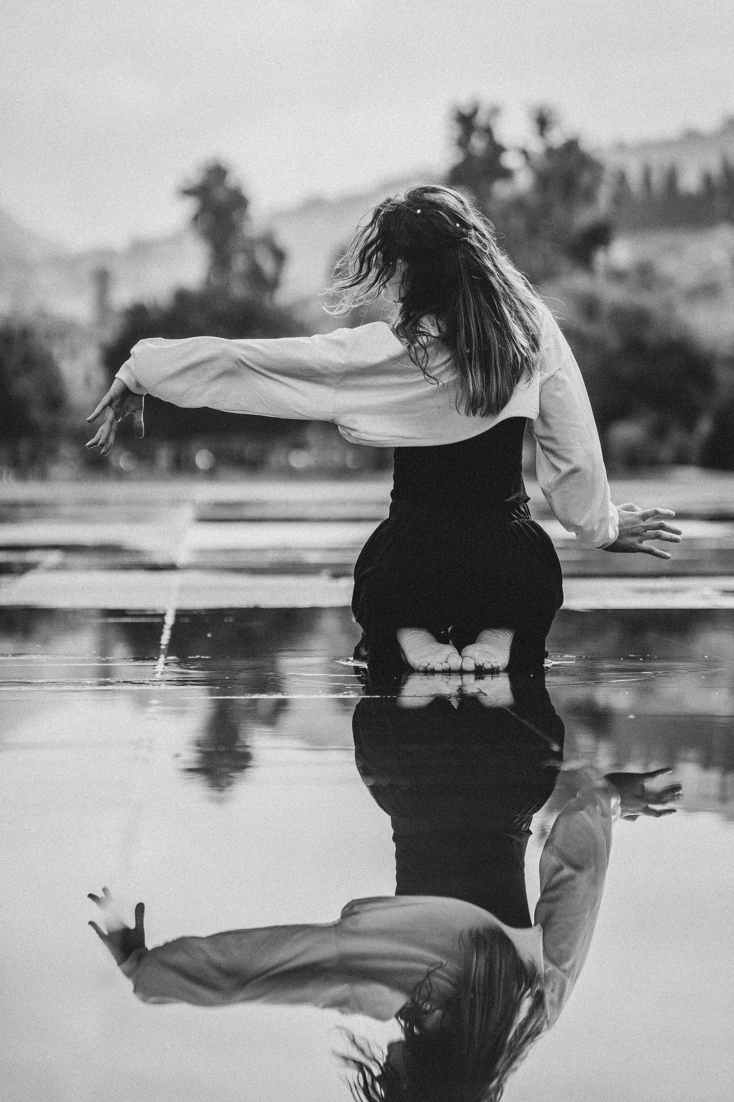 Woman in white shirt dancing in shallow water with reflection visible on wet surface.