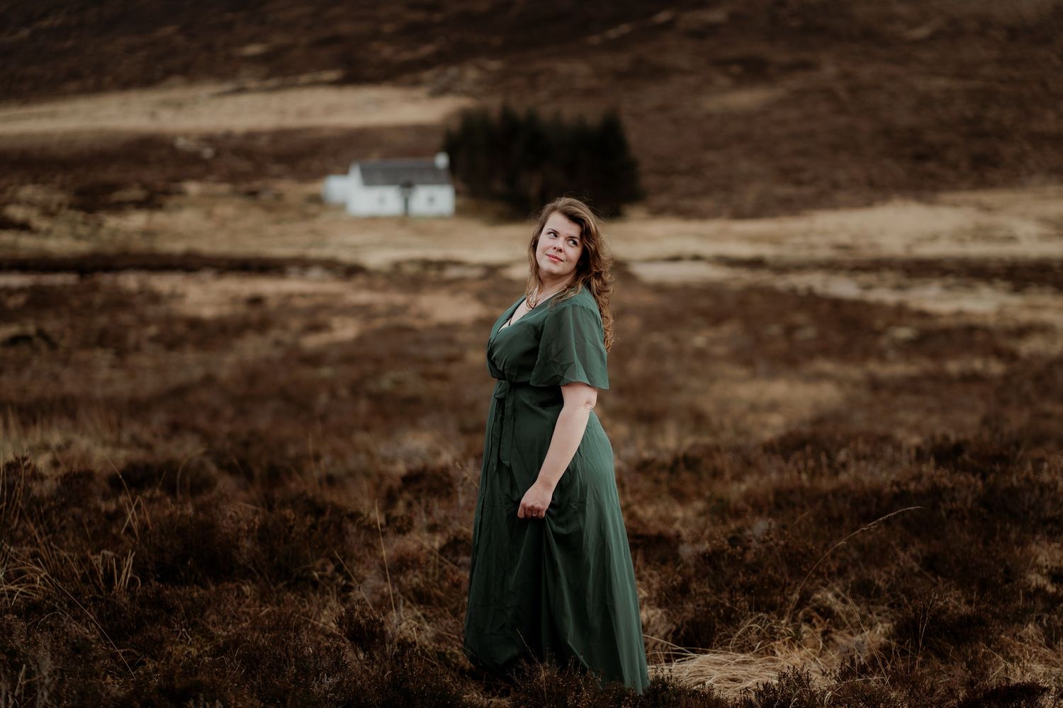 Person in emerald green dress twirls gracefully against a rugged mountainous landscape at sunset.
