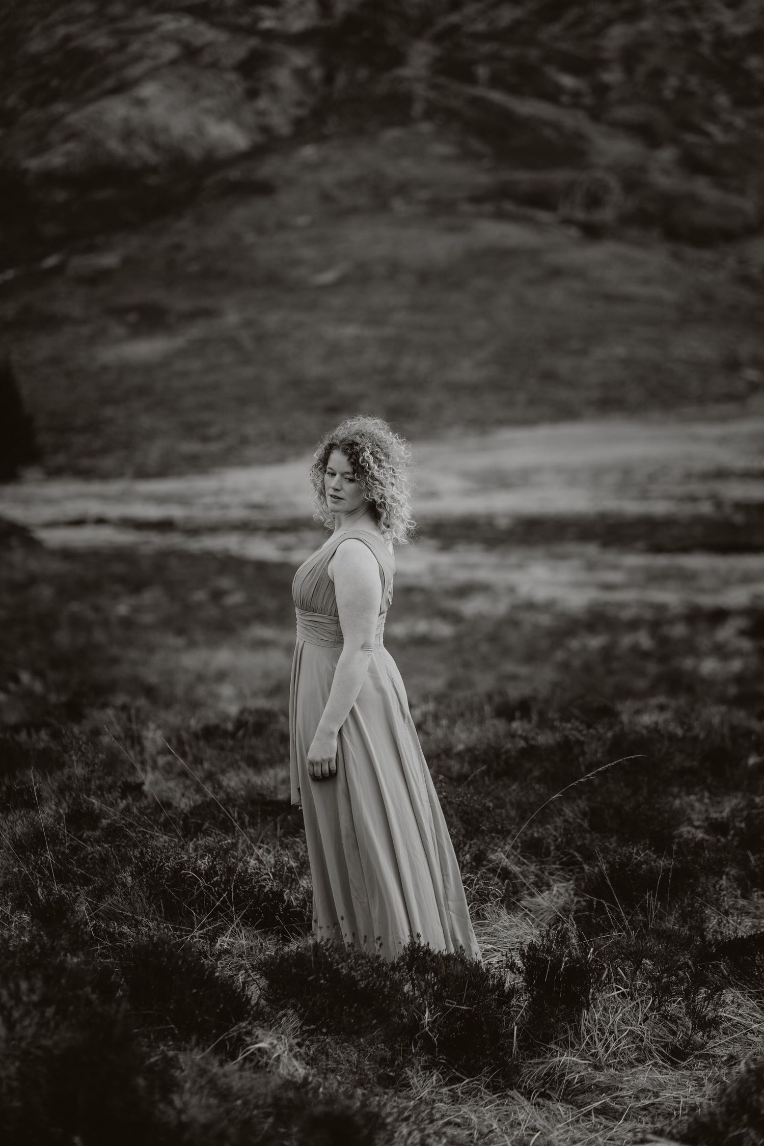 Dramatic black and white portrait of a figure in a flowing dress standing on a misty hillside.
