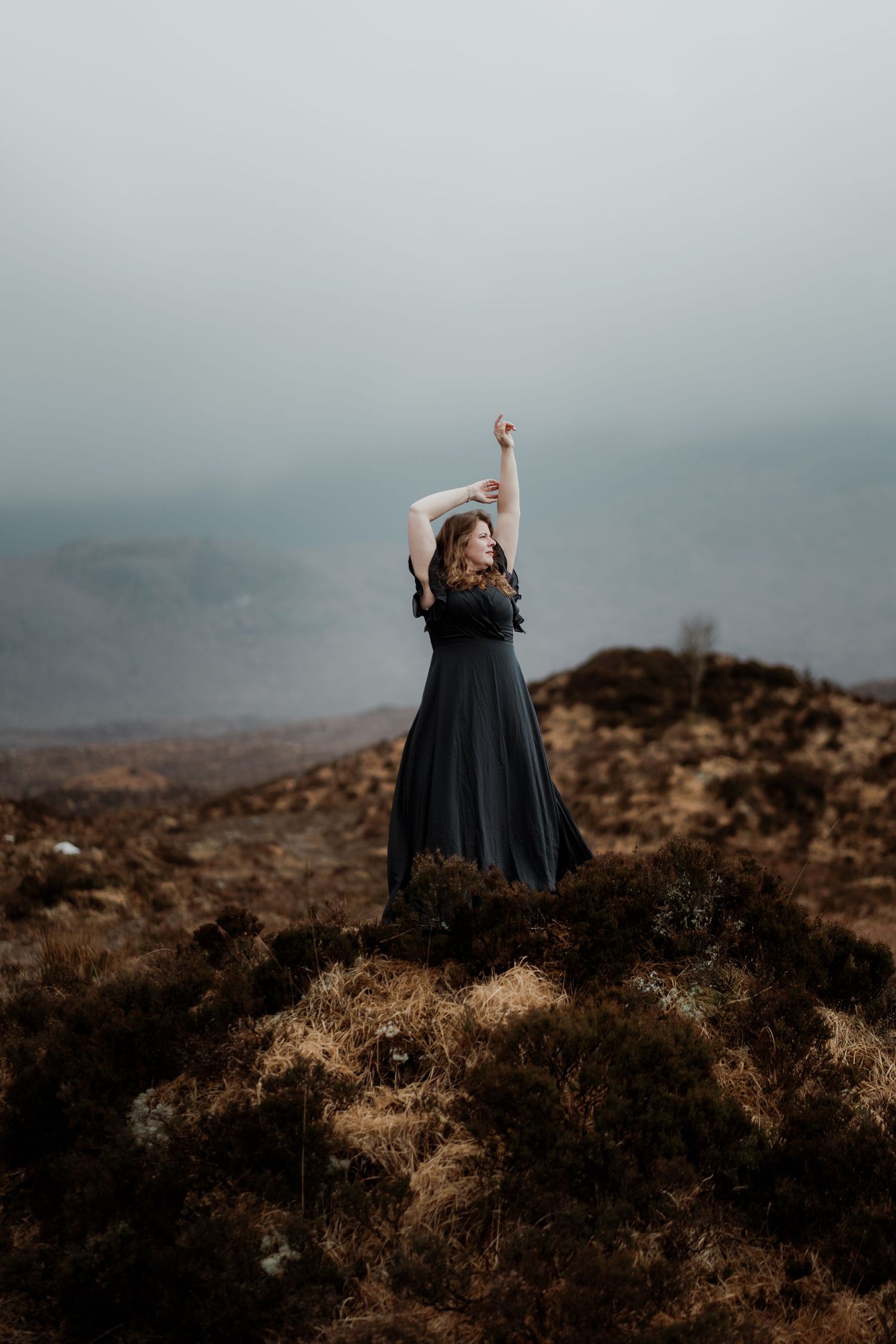 A series of progressive photos showing a figure in a flowing black dress dancing dramatically against a misty hillside landscape.
