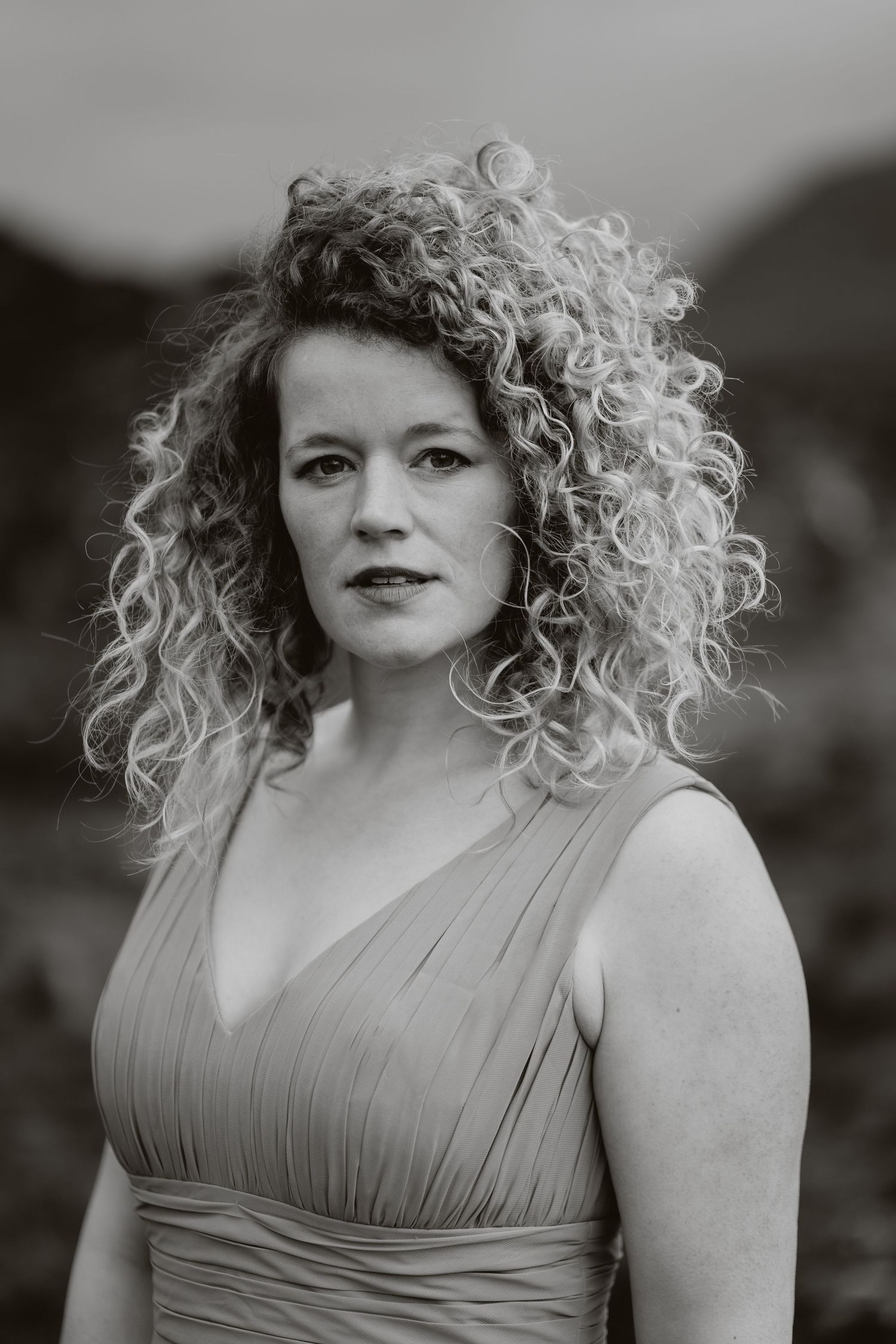 Black and white portrait showcasing natural curly hair against dramatic mountain landscape.