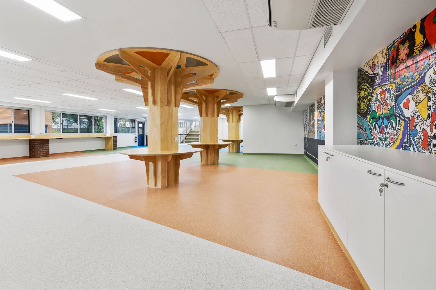 Interior photograph of a school or community space with a sculptural timber feature and colourful mural.