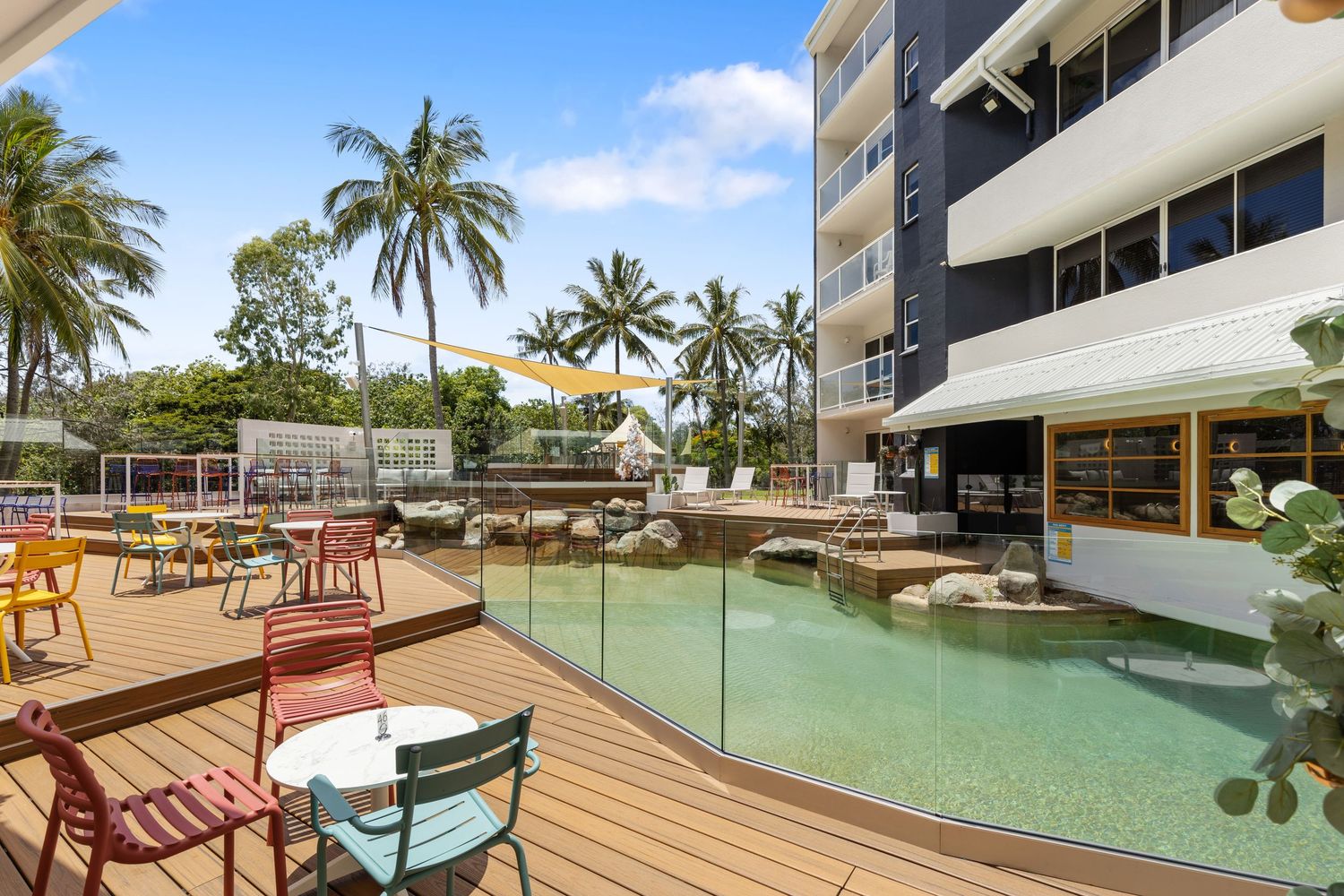 Photograph of a resort swimming pool deck with palm trees and building facade.