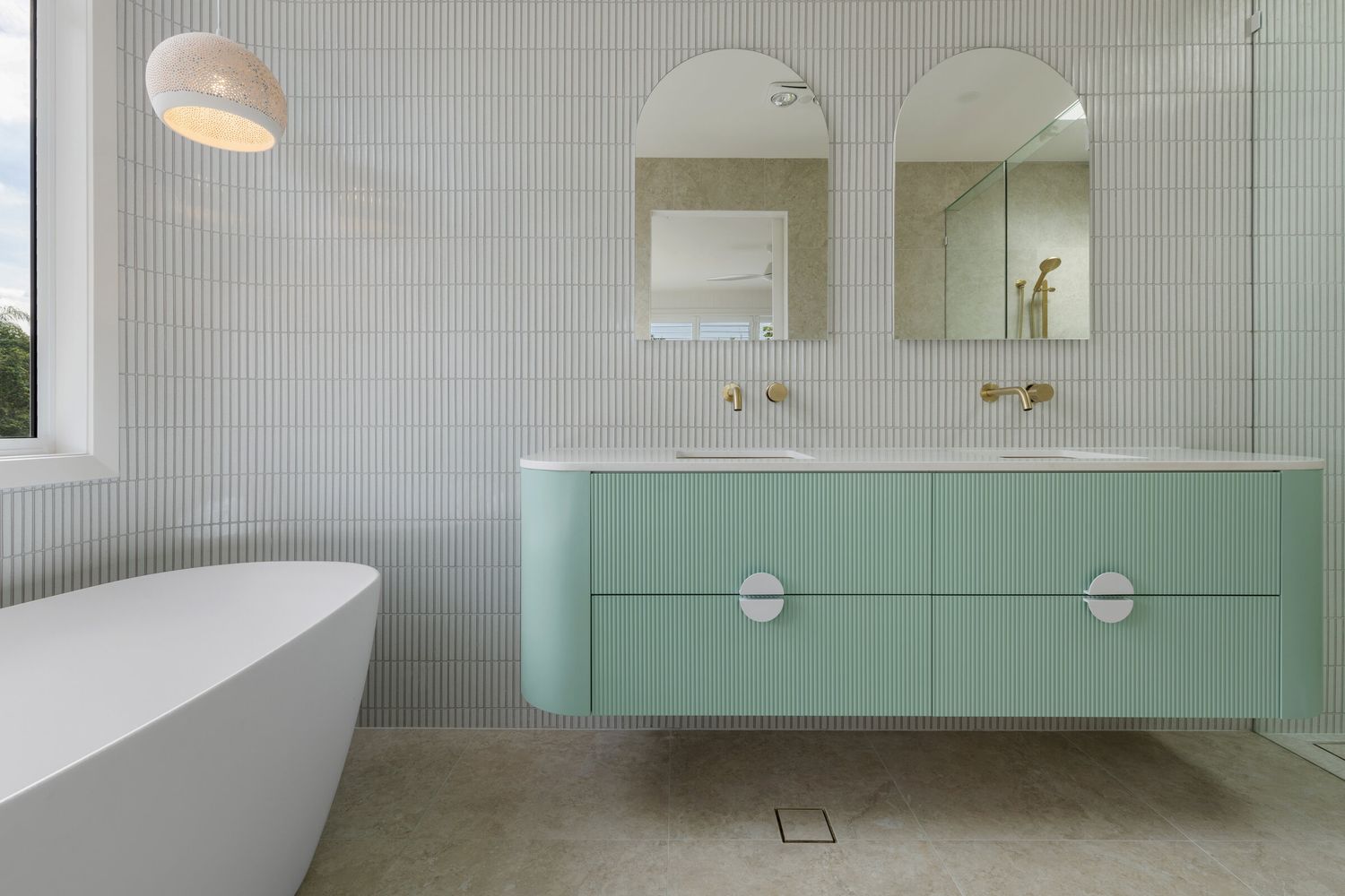 Interior photograph of a modern bathroom with teal vanity and freestanding bath.