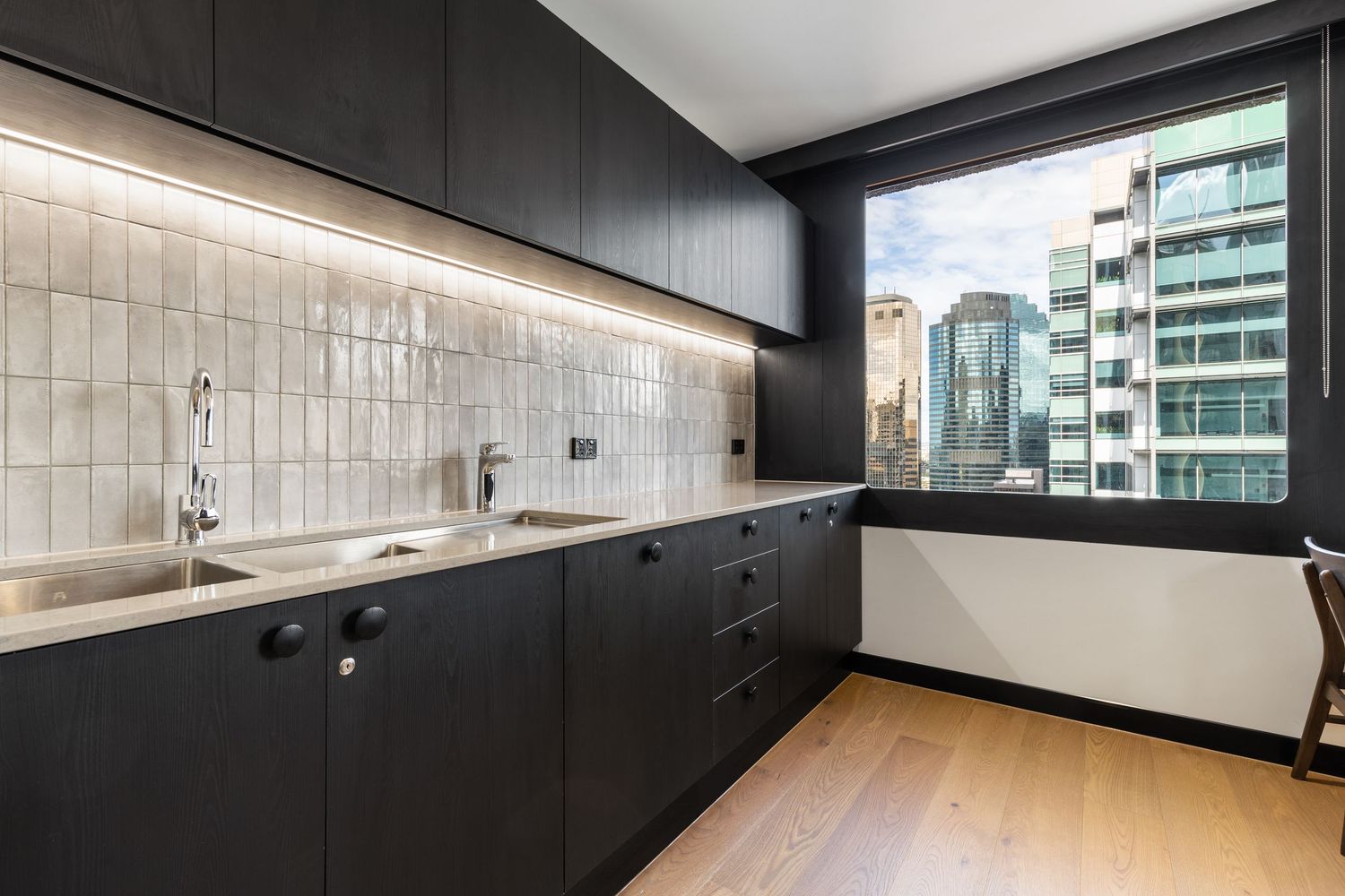 Interior photograph of a dark-toned kitchen with city skyline views.