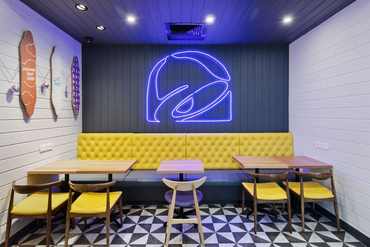 Interior photograph of a surf-themed bar with neon signage and yellow booth seating.