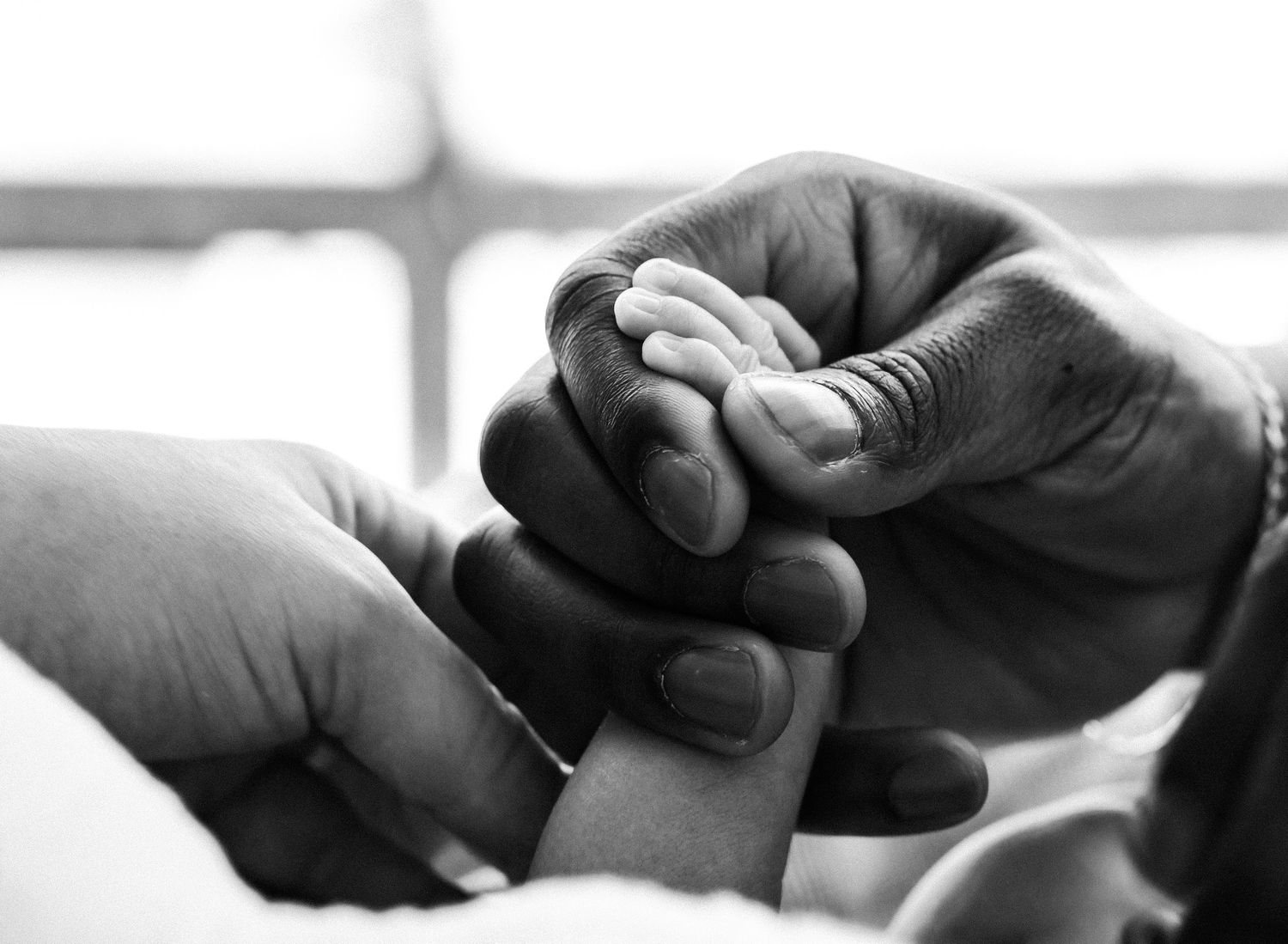 Black and white close-up of adult hands gently holding a tiny newborn baby hand, symbolizing love, family, and care.