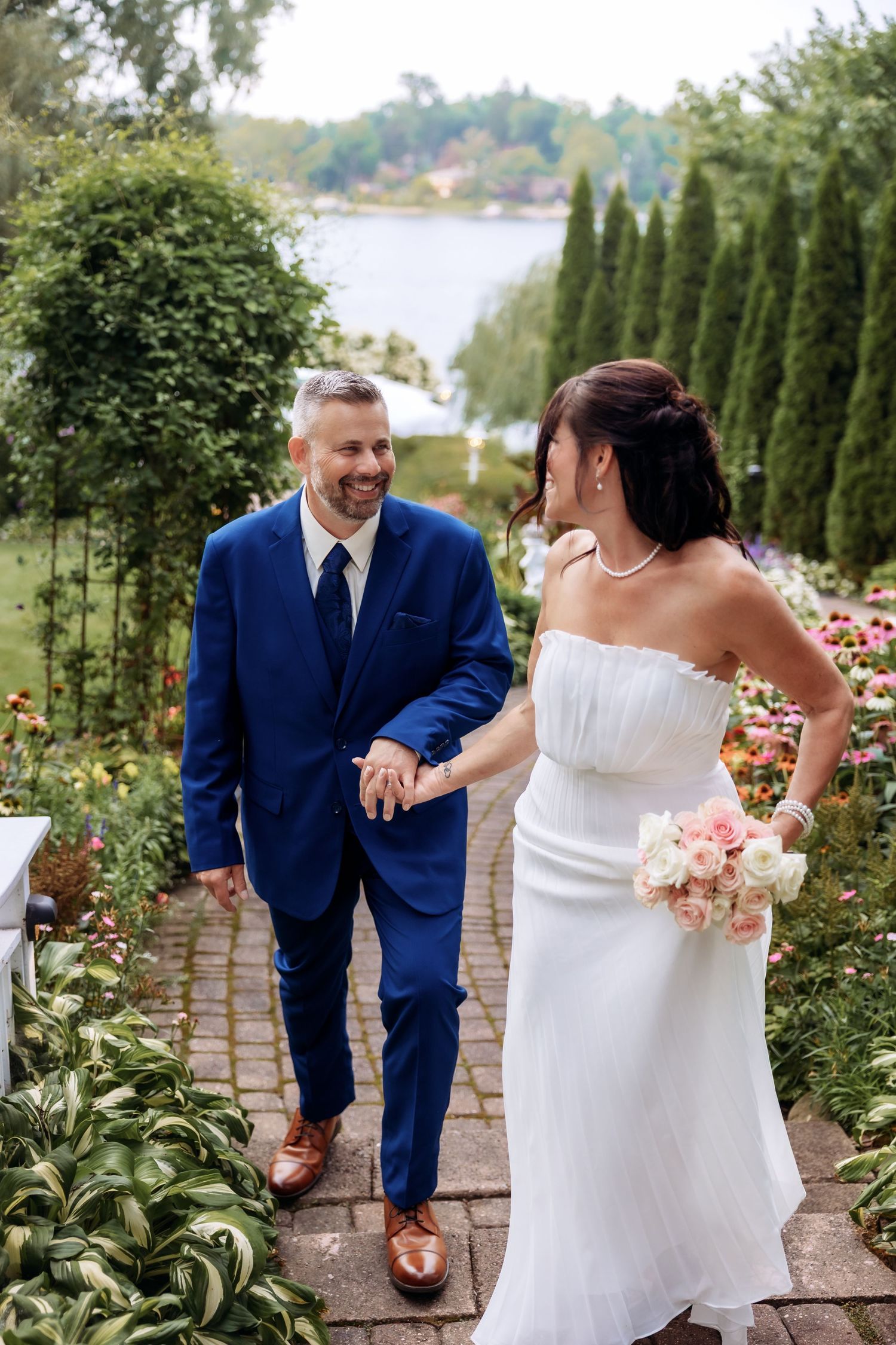 Couple walks up the path smiling at Victoria Wedding Chapel gardens by Rachel Martinez Photography, Michigan wedding photographer