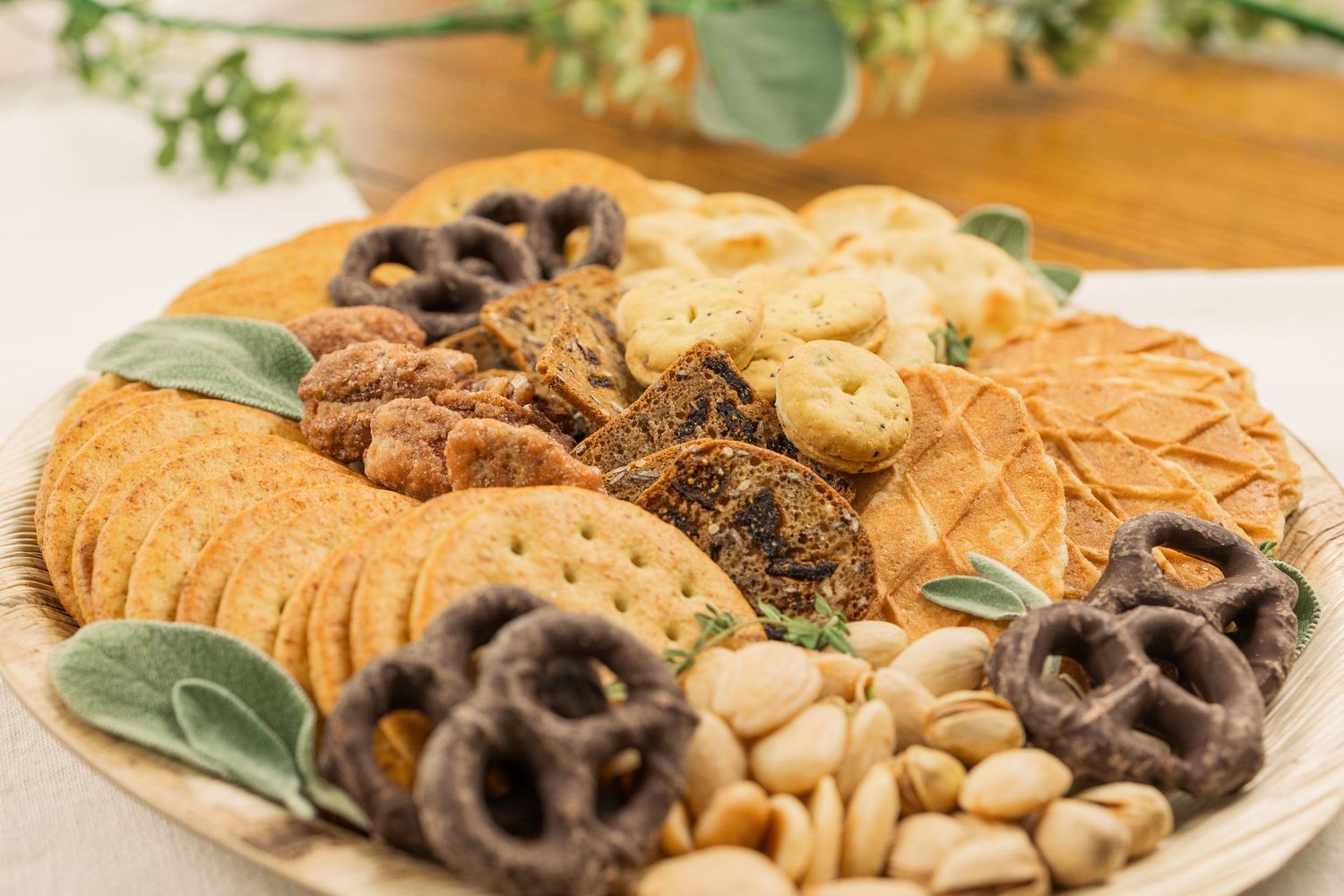 Gourmet cookie and dessert platter with variety of chocolates, nuts and pretzels arranged on wooden table.