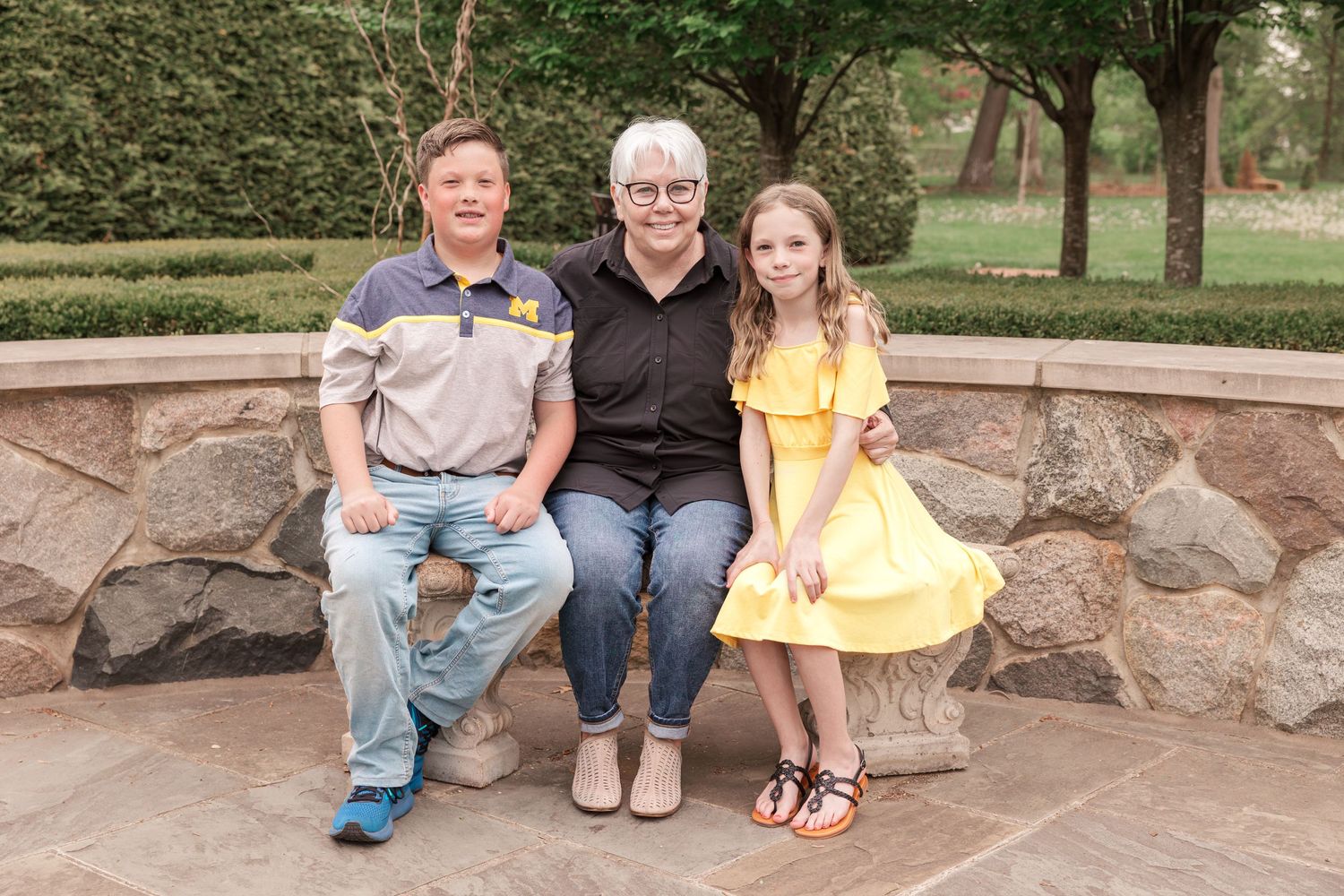 Three people sitting on stone bench in landscaped garden setting.