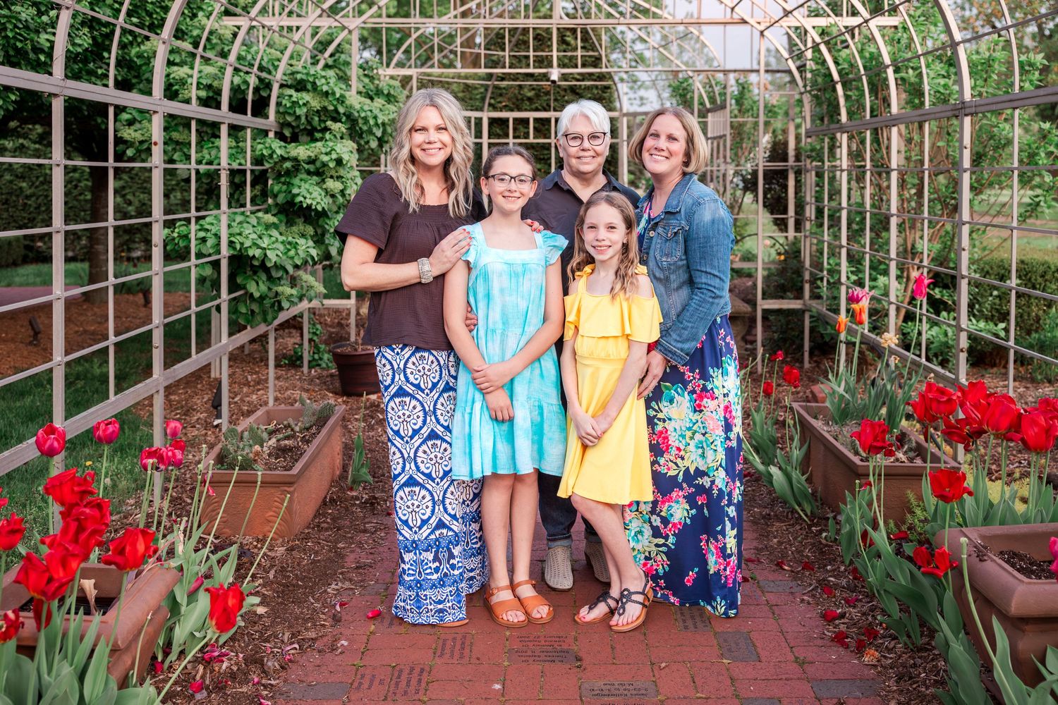 Family group photo in a garden tunnel with red flowers and climbing vines.