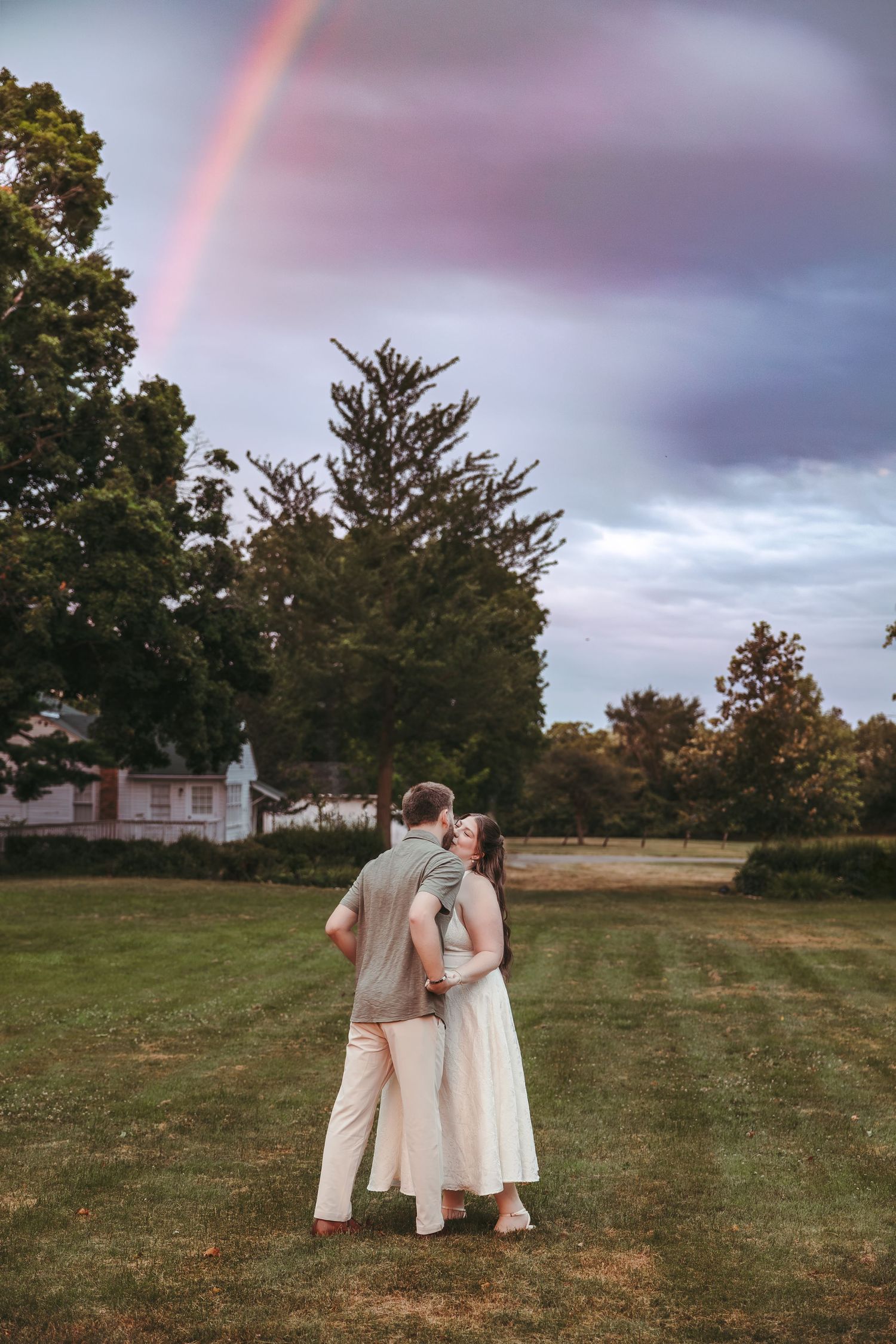 Couple embraces in a field under a rainbow at Greenmead Livonia by Rachel Martinez Photography, Michigan Wedding Photographer