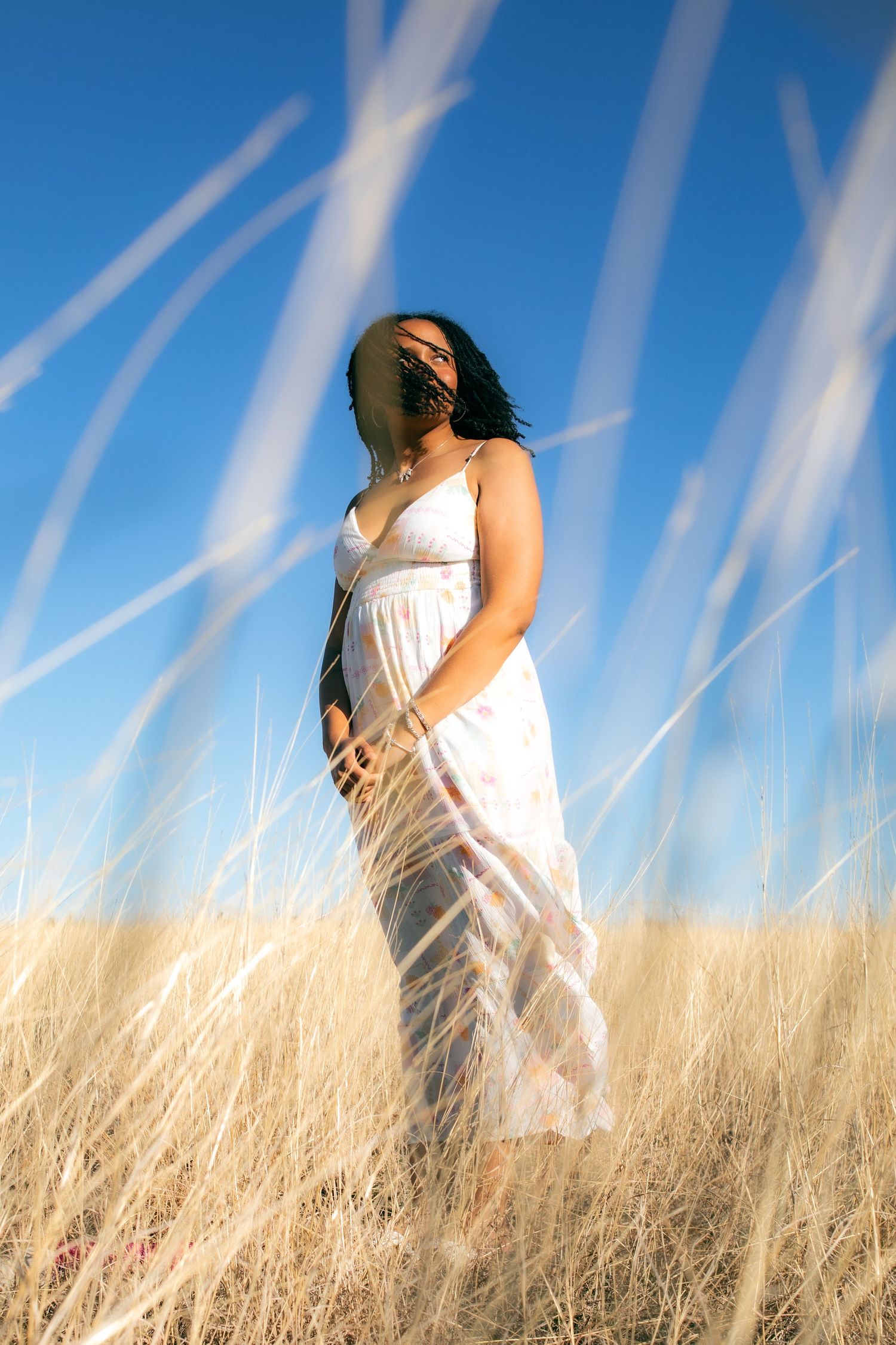 Woman in white sundress standing in golden dry grass field under blue sky.
