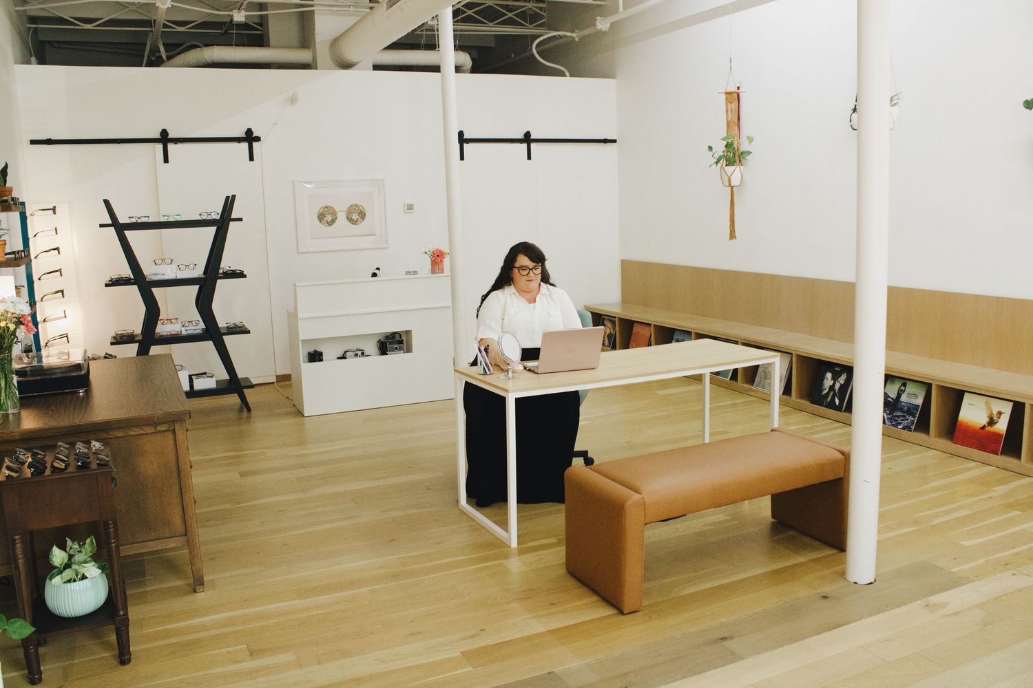 Woman standing at modern white desk in open concept office space with wood floors and barn doors.