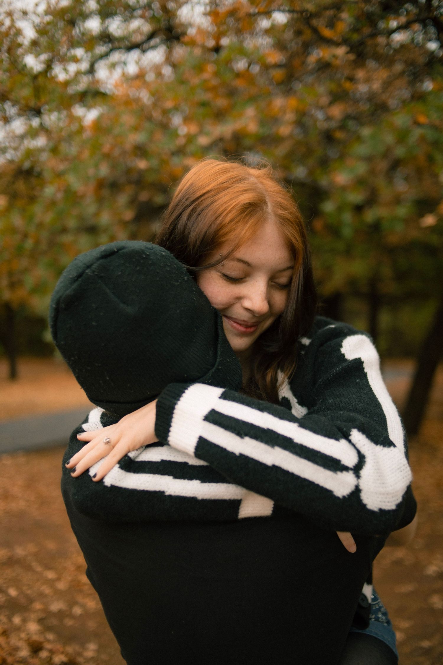 A smiling redhead woman hugging someone in a skeleton hoodie in an autumn park.