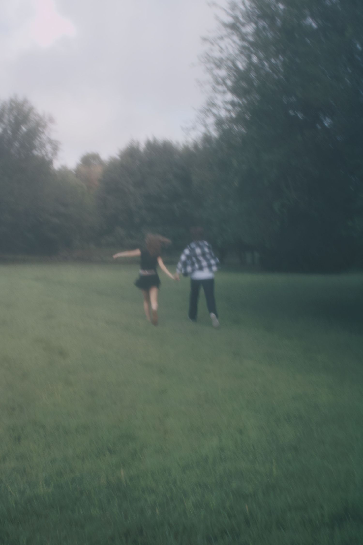 Blurred photo of couple holding hands running together across a lush green field.