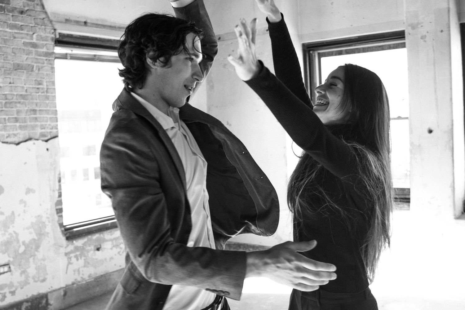 Black and white photo of a playful couple dancing and laughing together in a rustic industrial space.