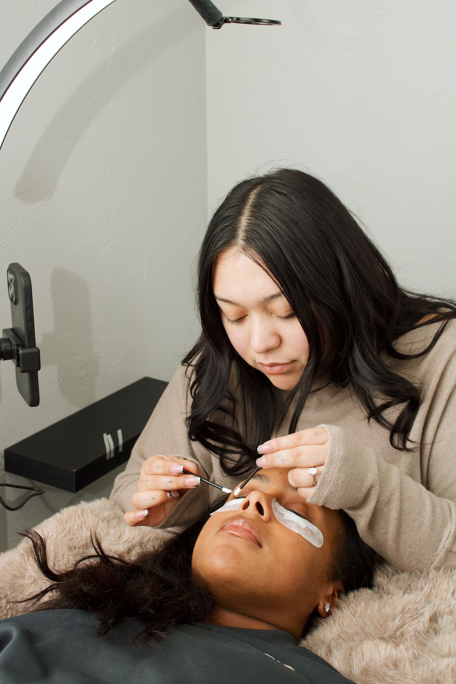 Esthetician applying eyelash extensions to a client lying down in a professional beauty salon.