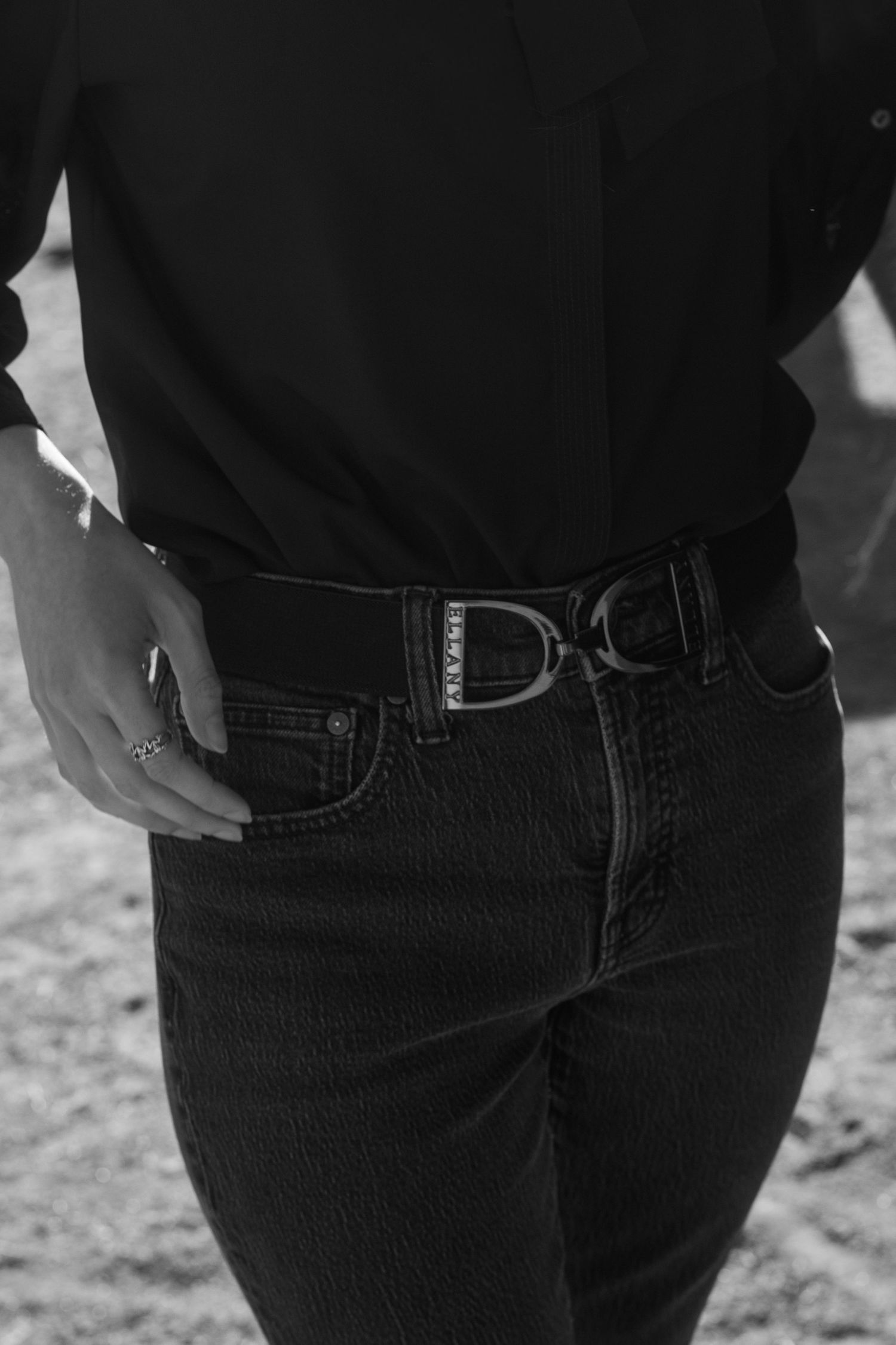 Black and white close-up of woman wearing black D-ring belt with black shirt and dark jeans.