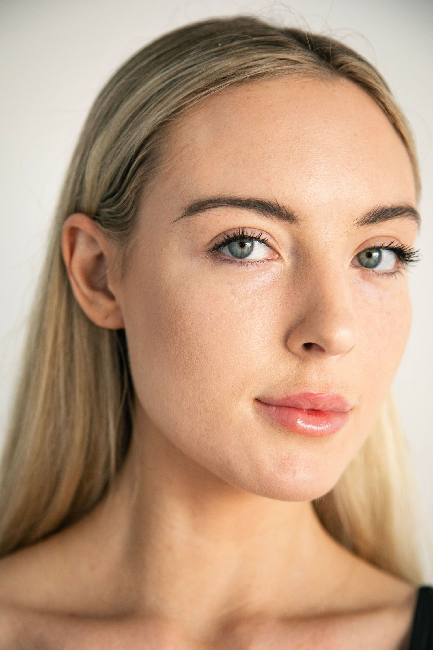 Close-up portrait of a blonde woman with blue eyes and natural makeup against a white background.