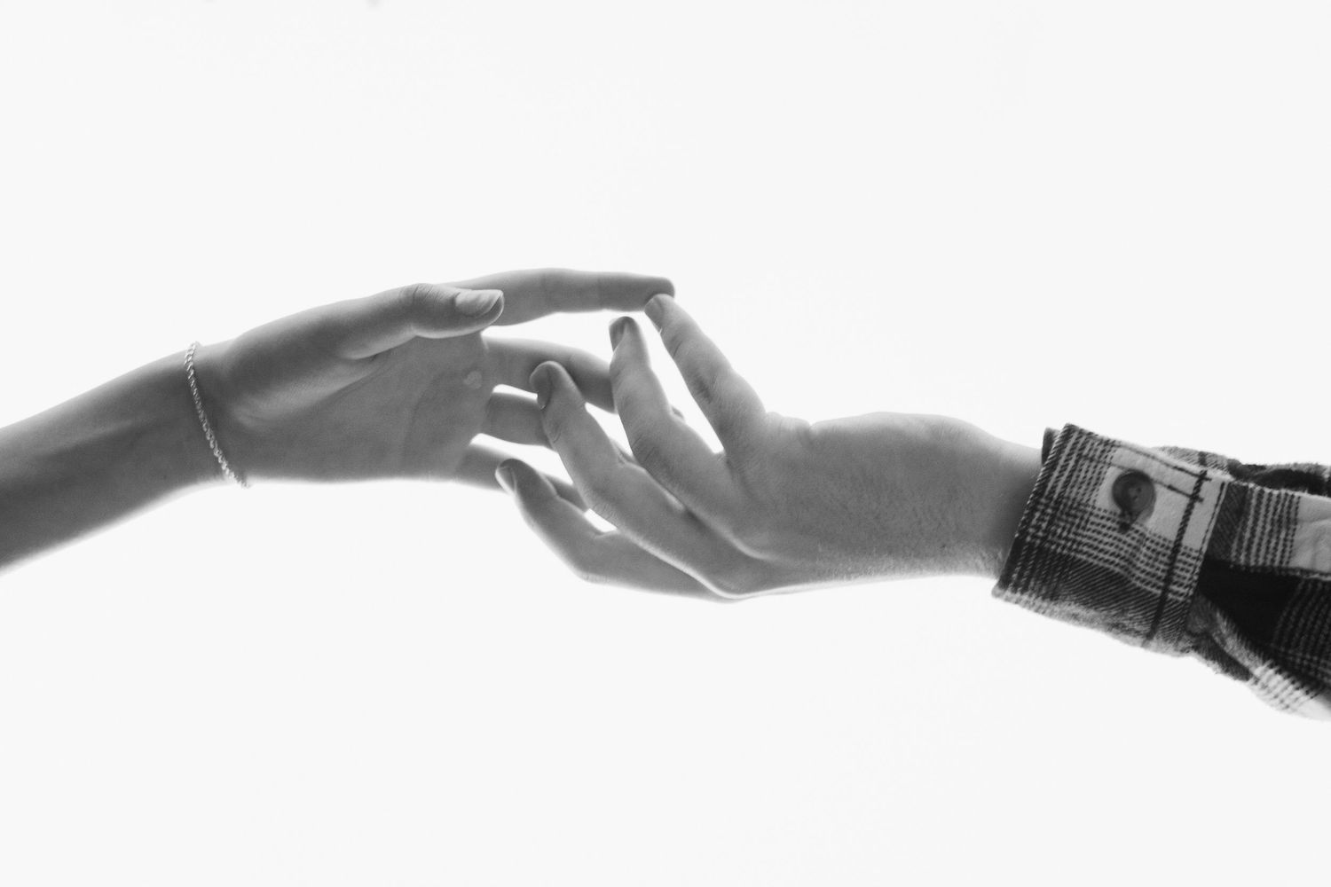 Black and white image of two hands gently reaching toward each other on white background.