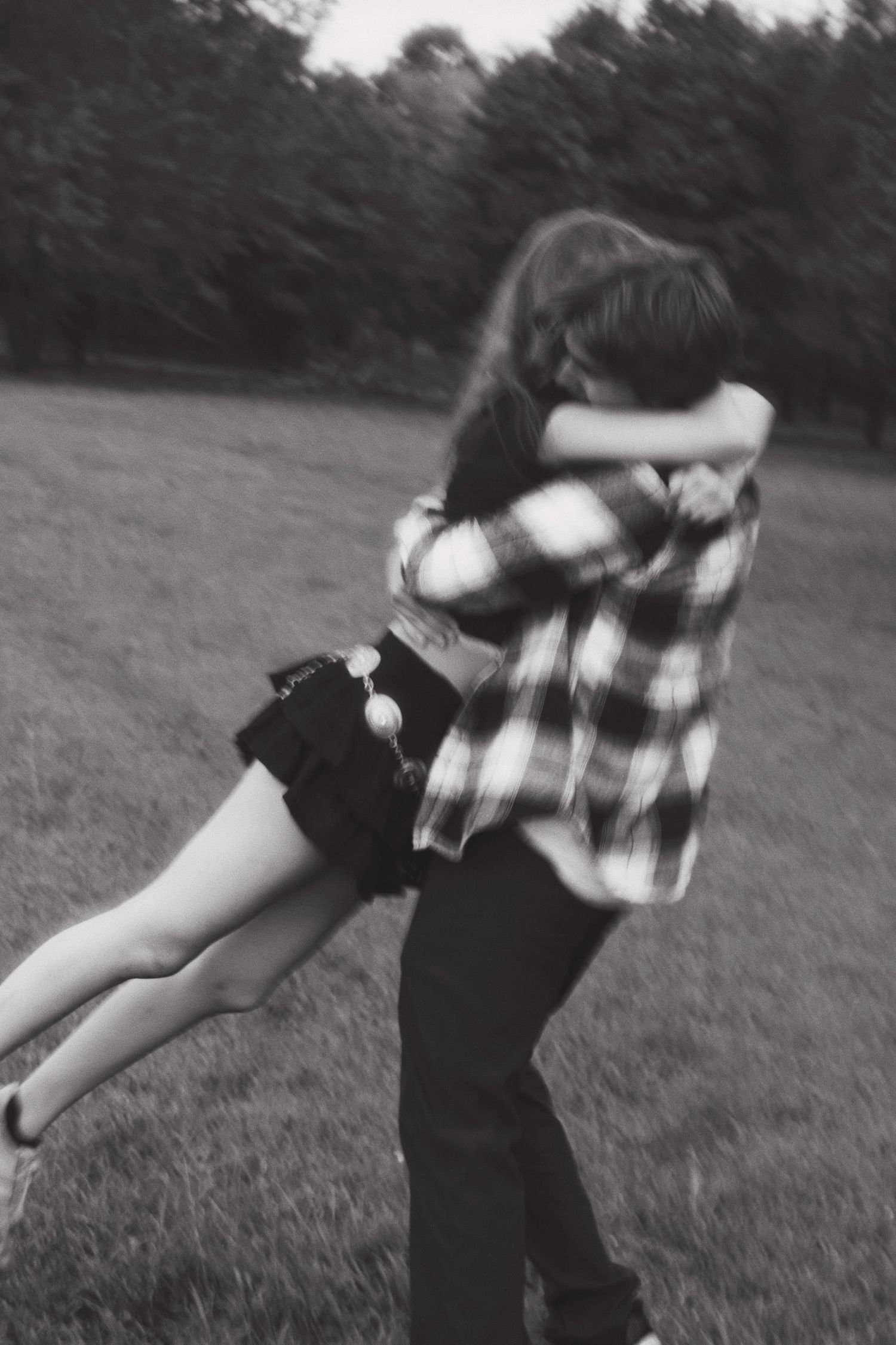 Black and white photo of couple embracing as man lifts woman in an open grassy field.