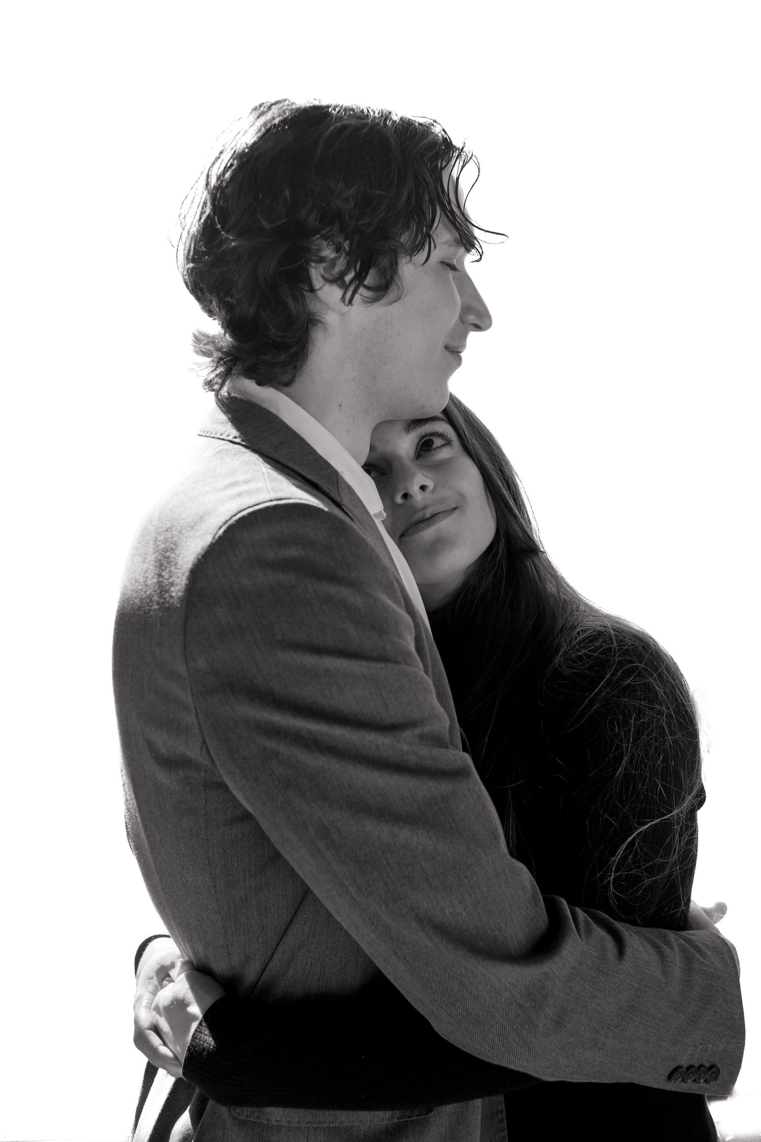 Black and white portrait of a woman leaning against a man in a suit jacket against a white background.