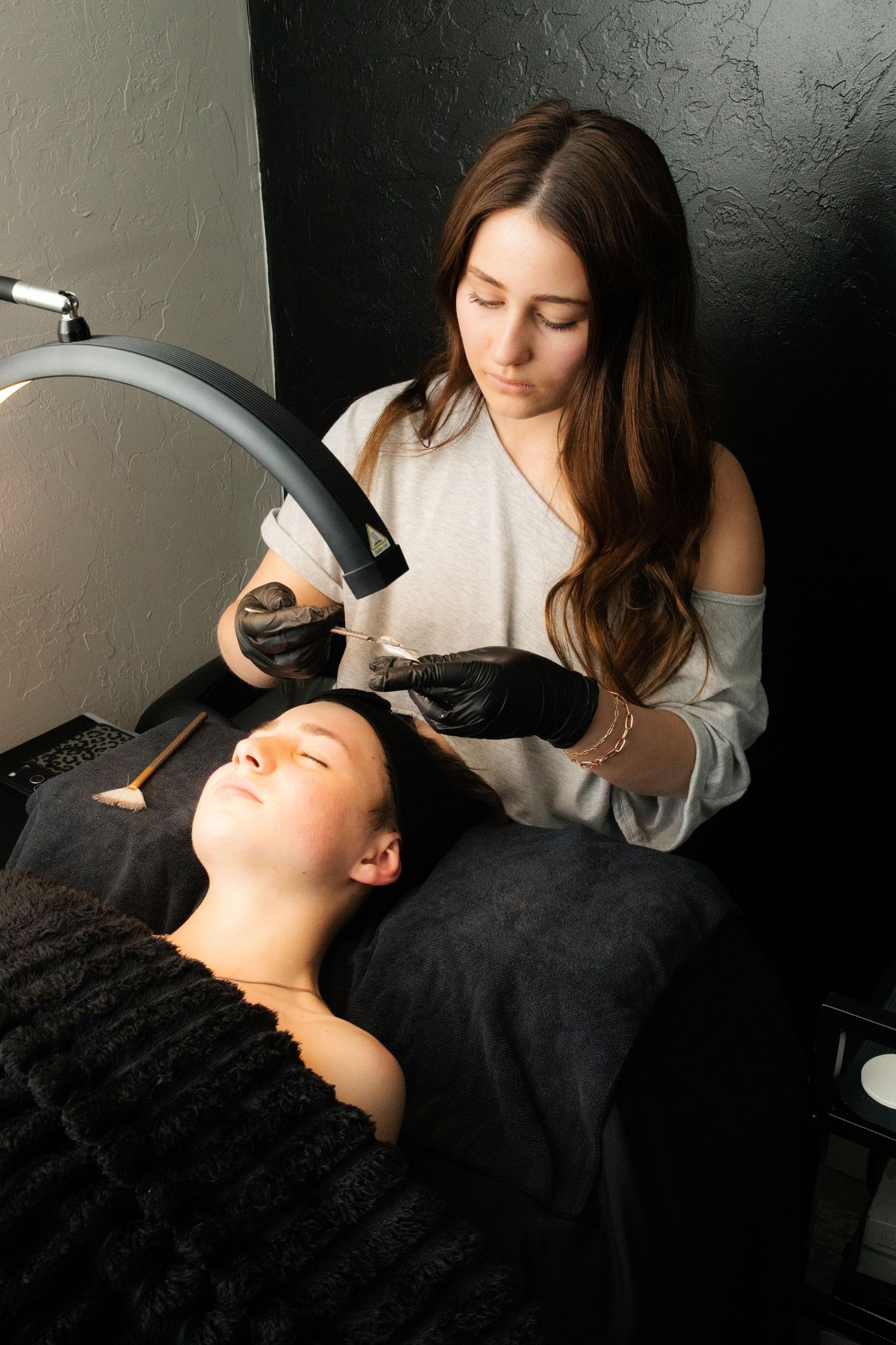Beauty professional applying facial treatment to relaxed client in dark salon setting.