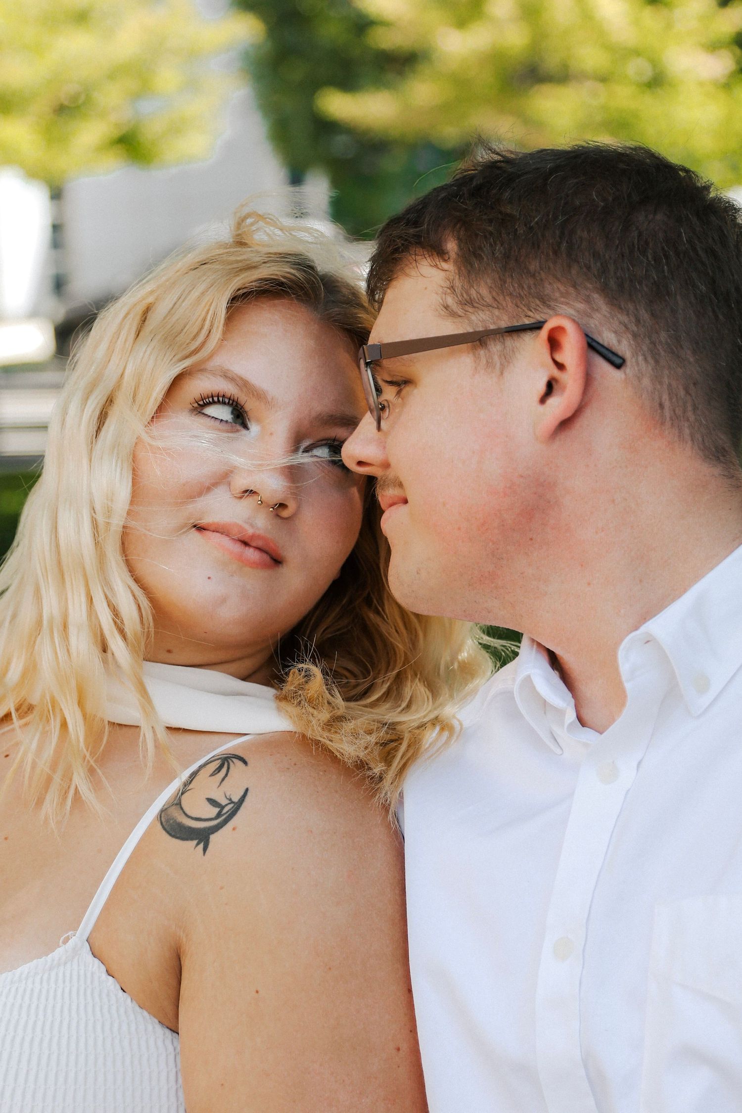 Close-up of a smiling couple with a fish tattoo visible on the woman's shoulder, outdoors.