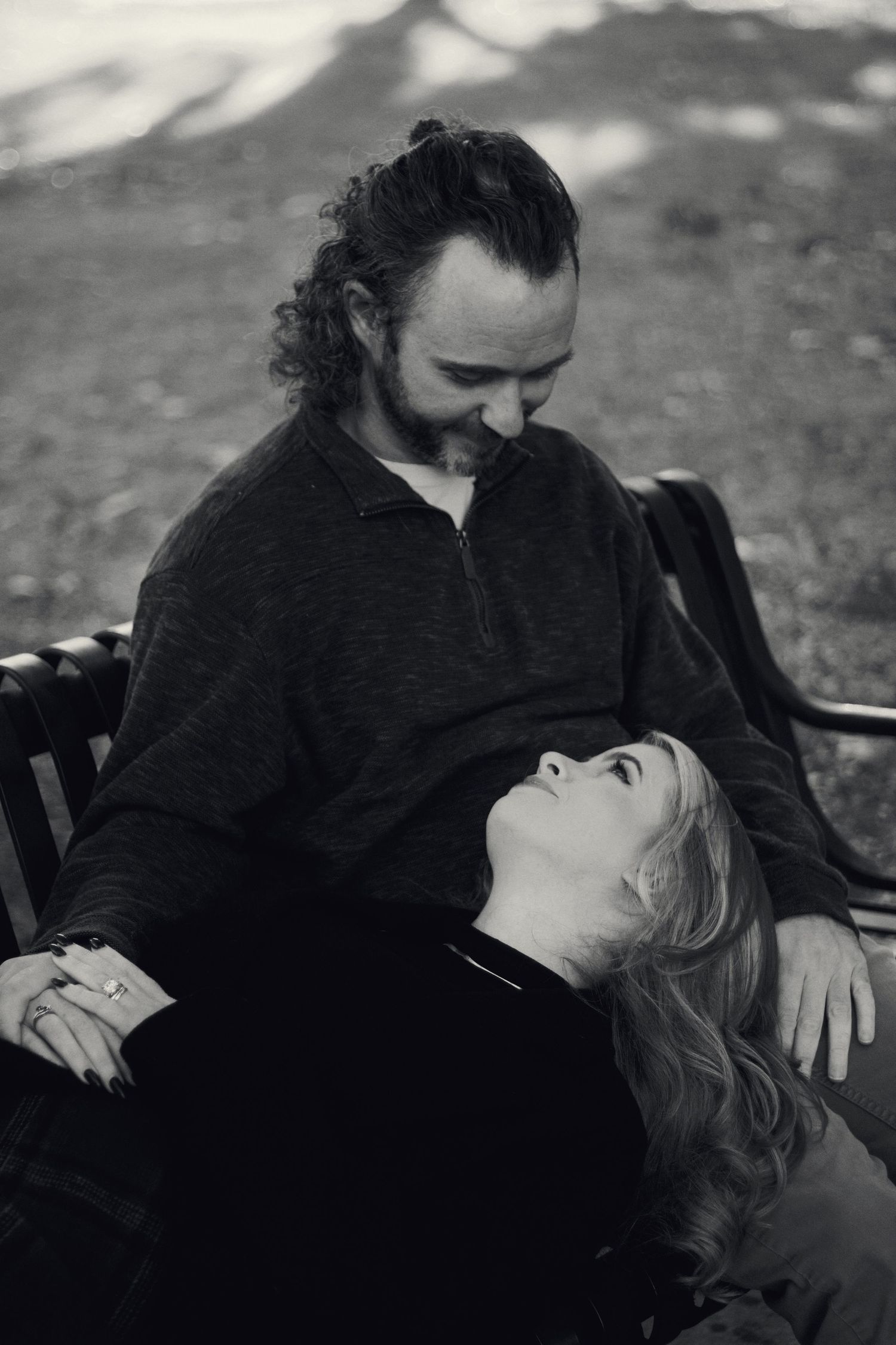 Black and white photo of a couple on a park bench, woman lying in mans lap gazing up at him lovingly.
