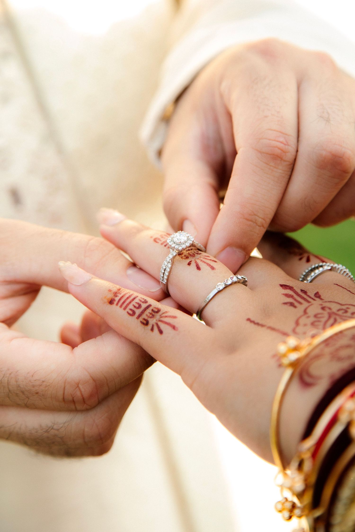 Close-up of groom placing diamond engagement ring on bride's henna-decorated hand at Indian wedding ceremony.
