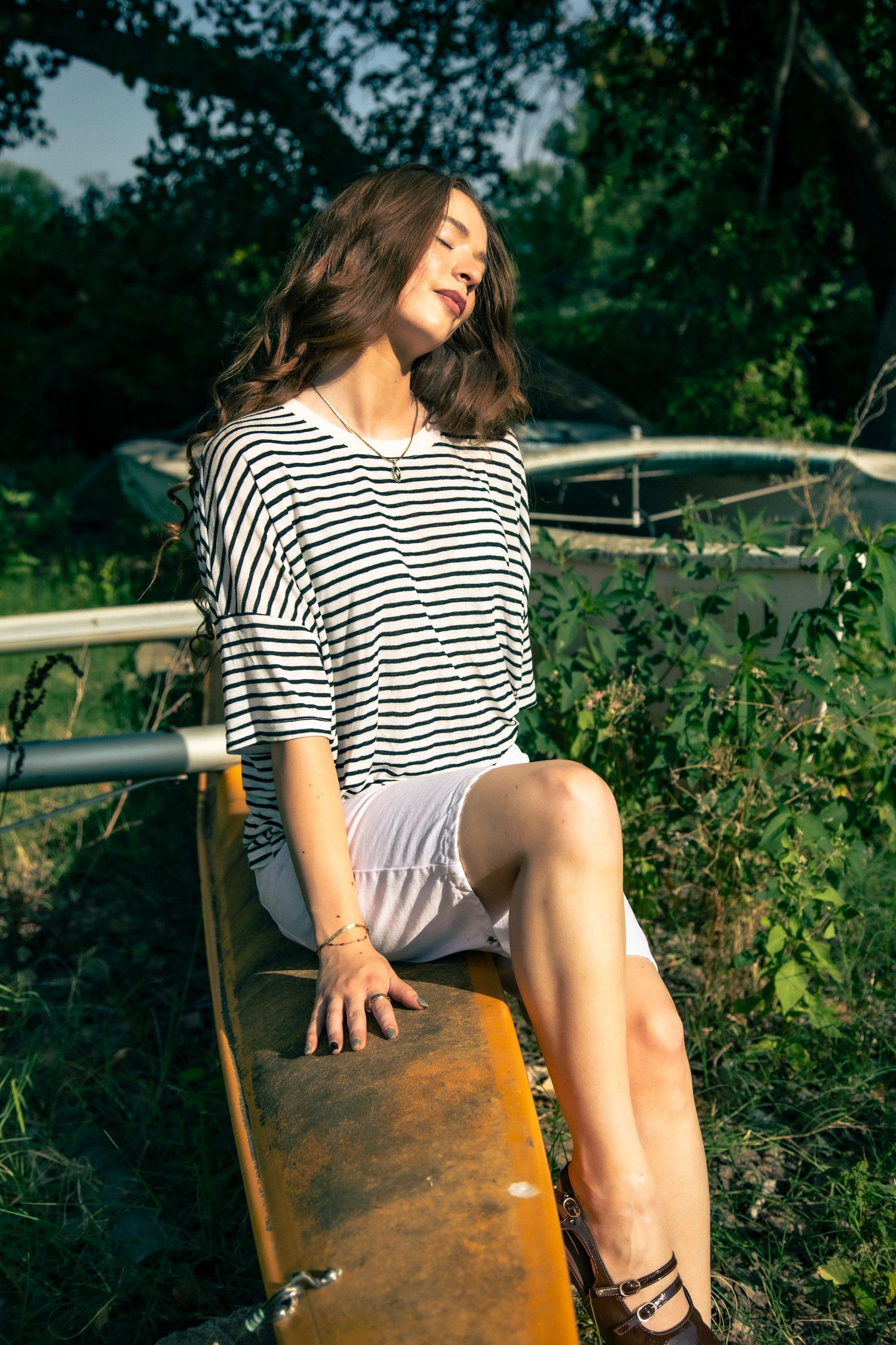 Young woman in striped shirt and white shorts sitting on vintage seesaw in sunlight.