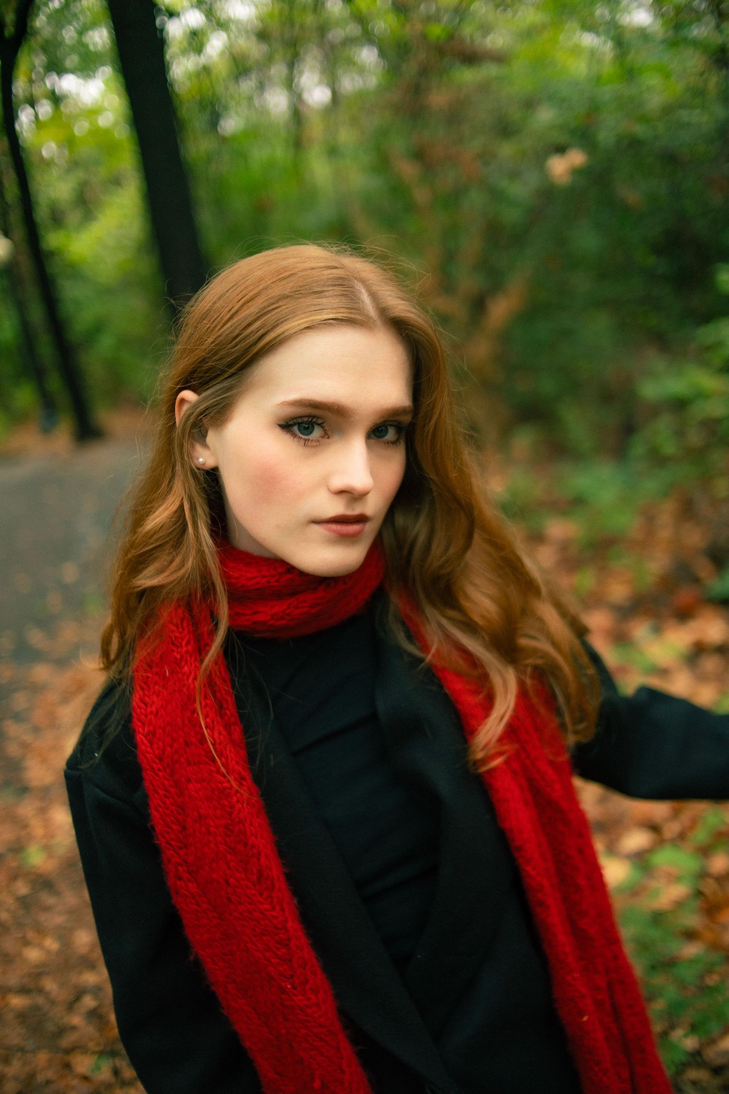 Young woman with red scarf and black coat standing on a forest path in autumn.