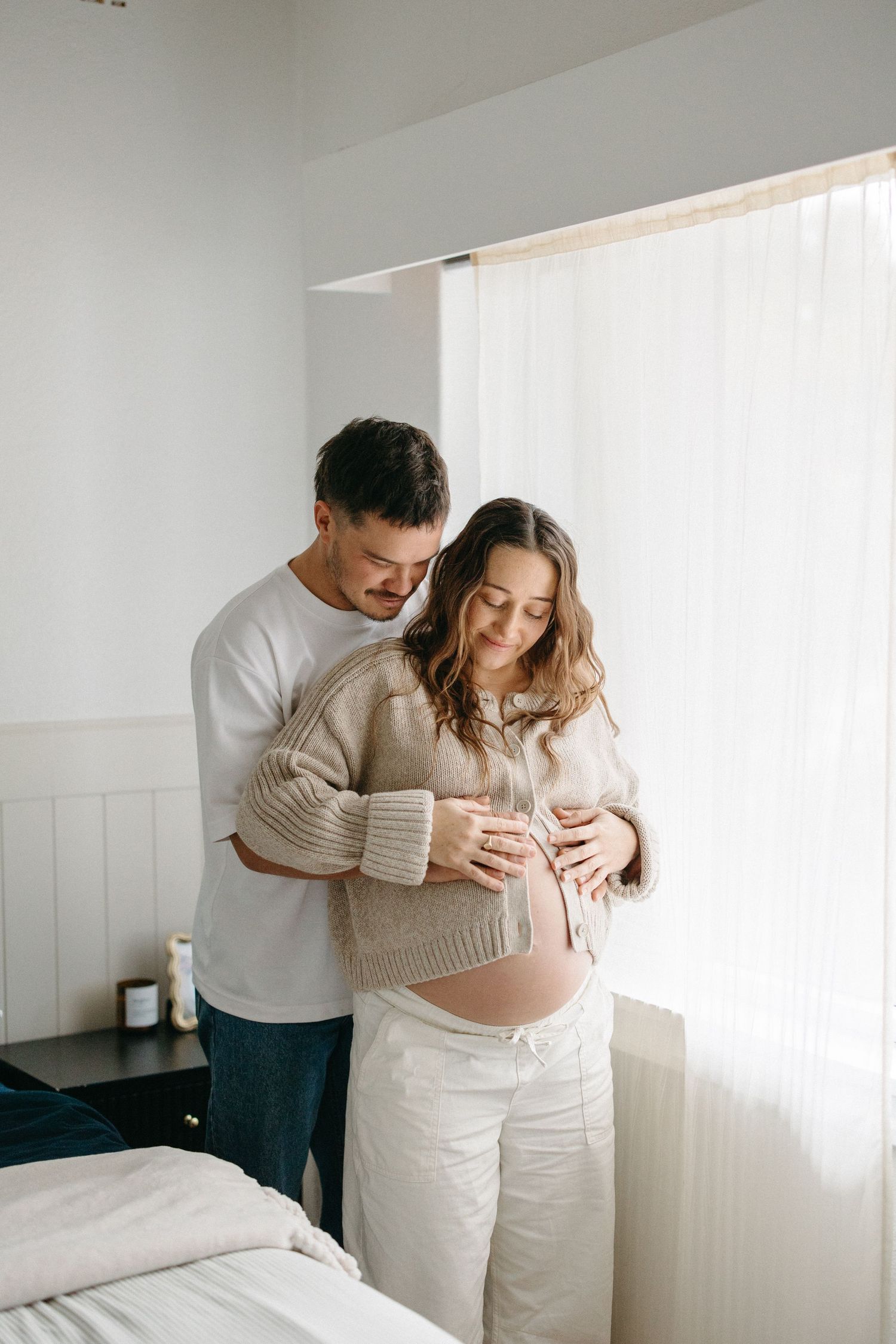Pregnant woman standing beside her partner in their bedroom