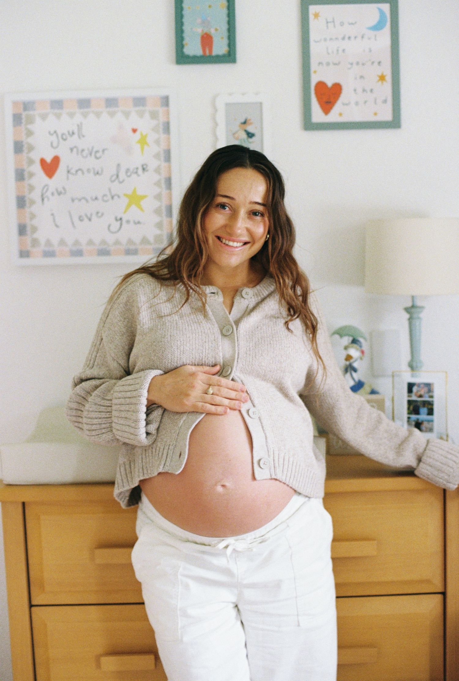 pregnant woman smiling at the camera in the baby's nursery captured on 35mm film