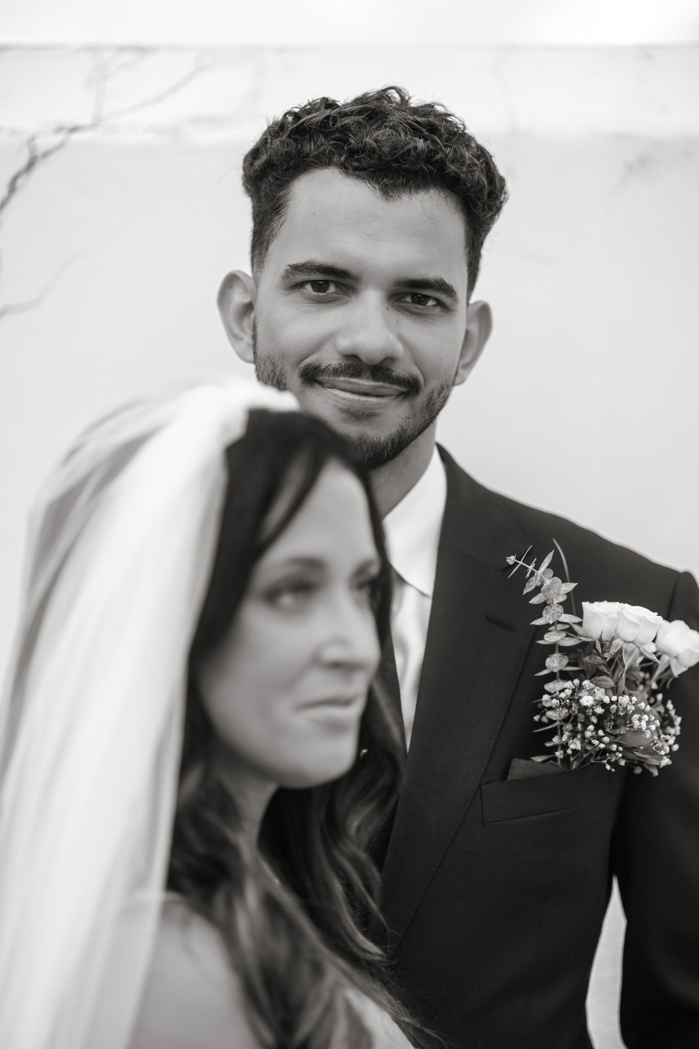 A black and white photograph of a bride and groom on their wedding day, with the groom wearing a boutonniere.