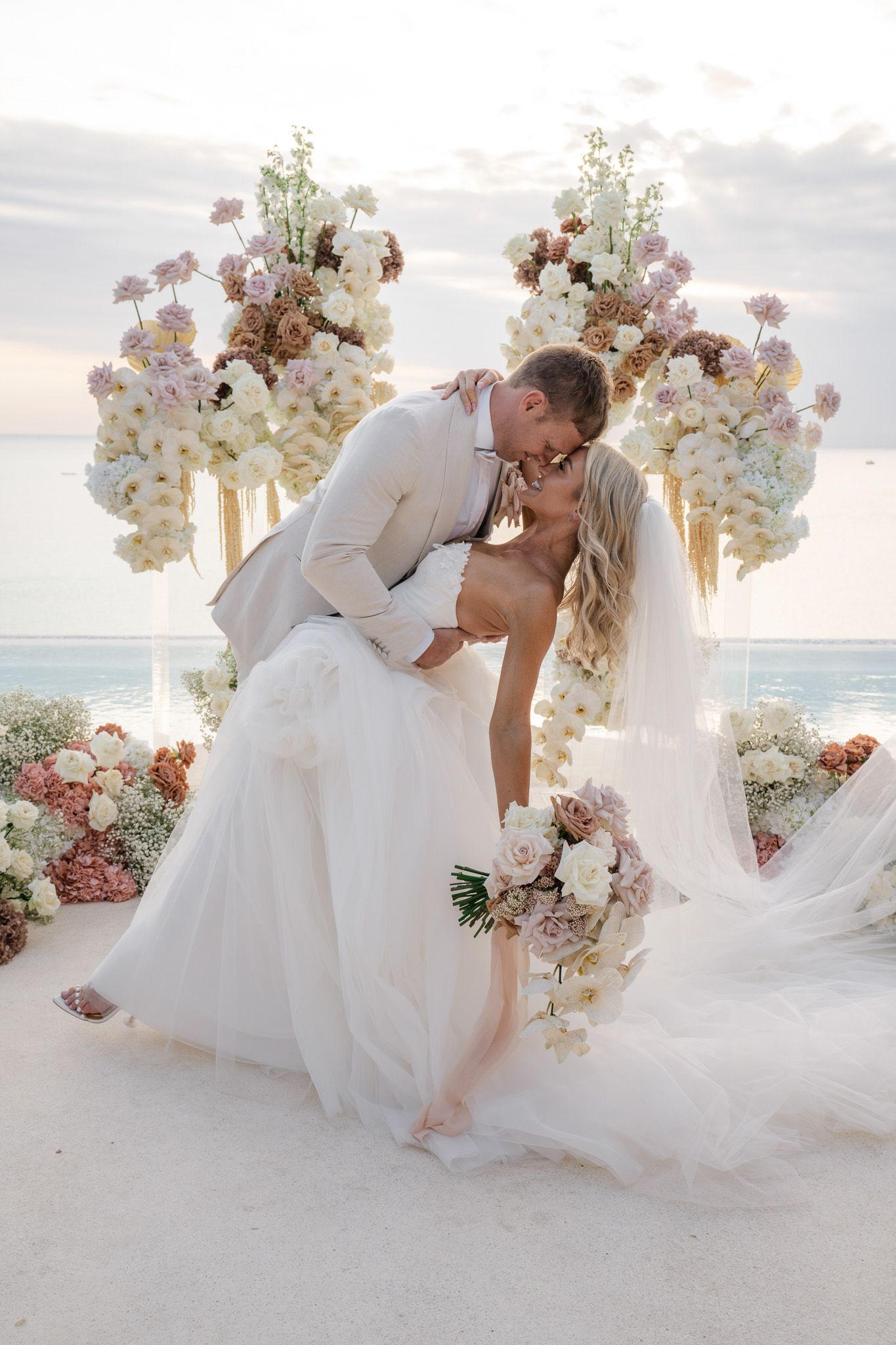Romantic beach wedding photo series showing couple in white dress and suit dipping and kissing against ocean backdrop.