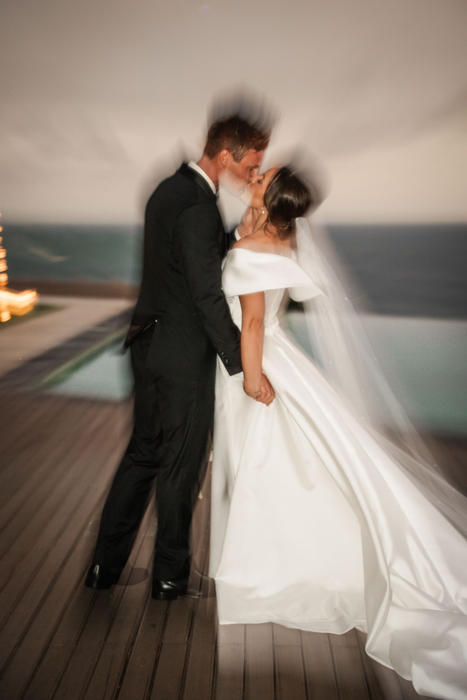 Motion-blurred wedding couple dancing on a wooden deck at sunset with dramatic flowing dress movement.
