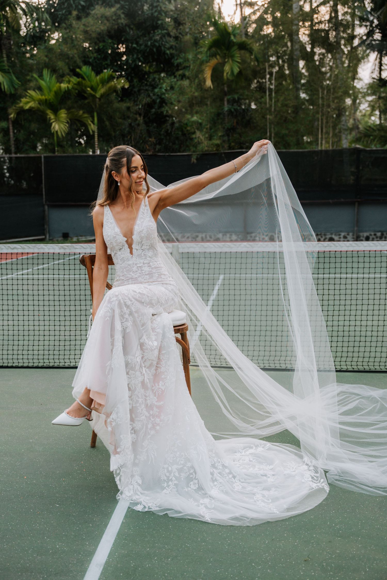 A flowing white lace wedding dress with long train and veil dramatically displayed on a tennis court in a series of poses.